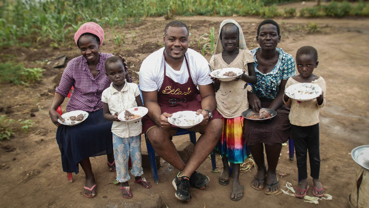Selasi sits surrounded by children and adults with plates of food