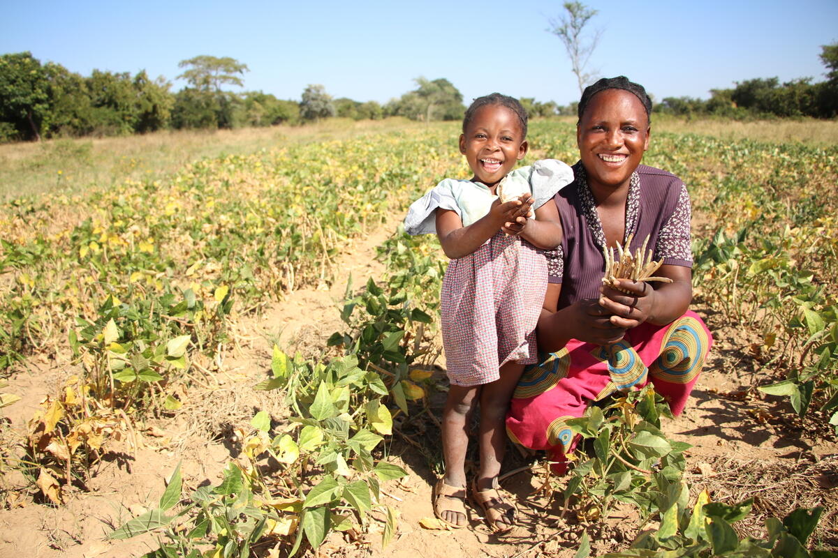 A man in Mozambique heaves a sack of food aid distributed rice onto his back whilst a World Vision staff member helps