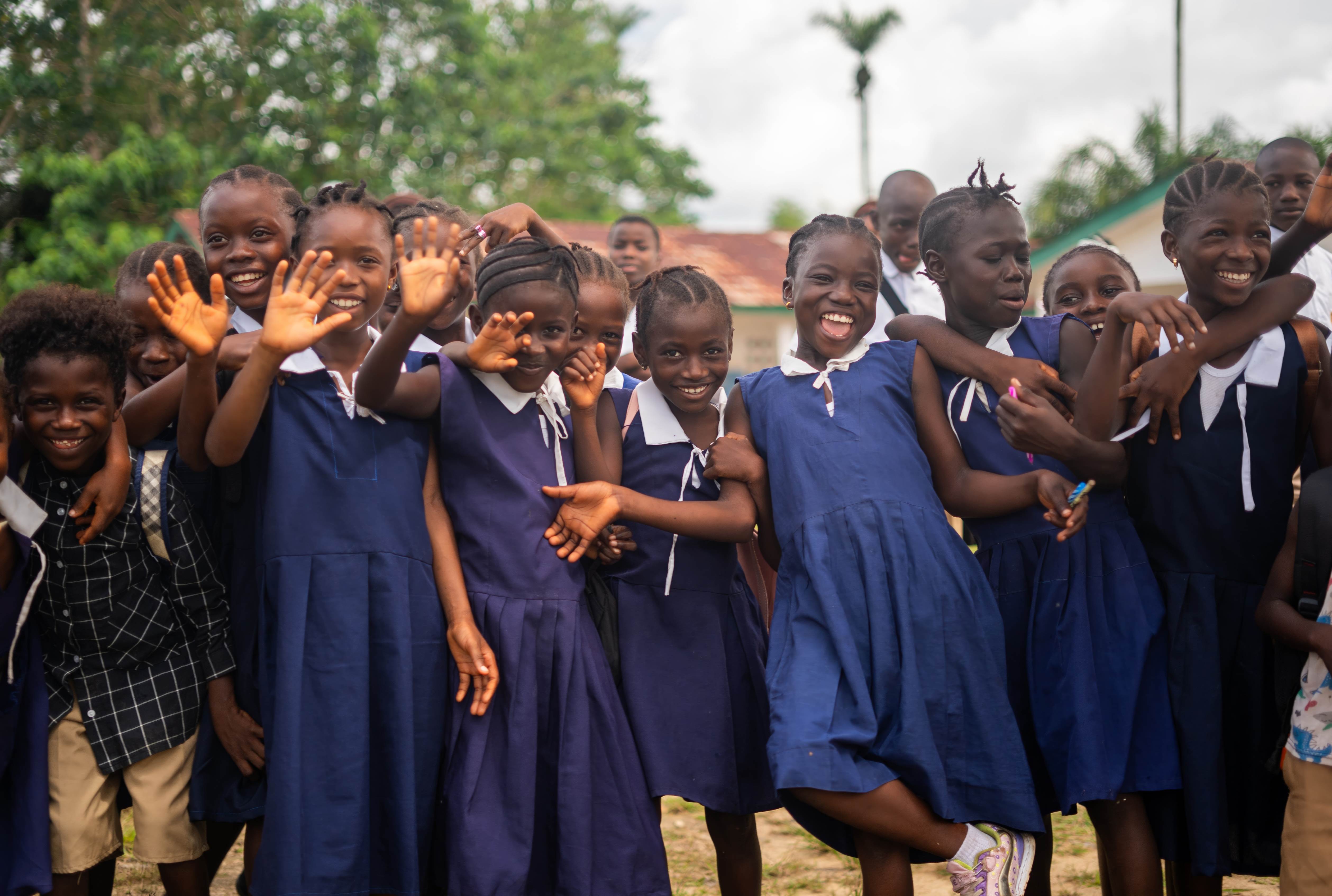 School girls wearing uniform, smiling and waving at the camera