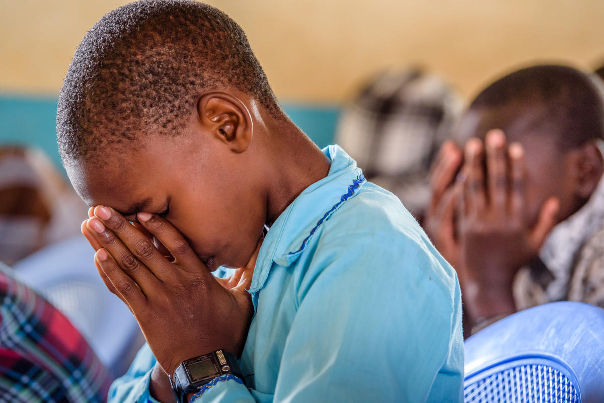 Photo taken side on of a boy from Kenya in a blue shirt praying