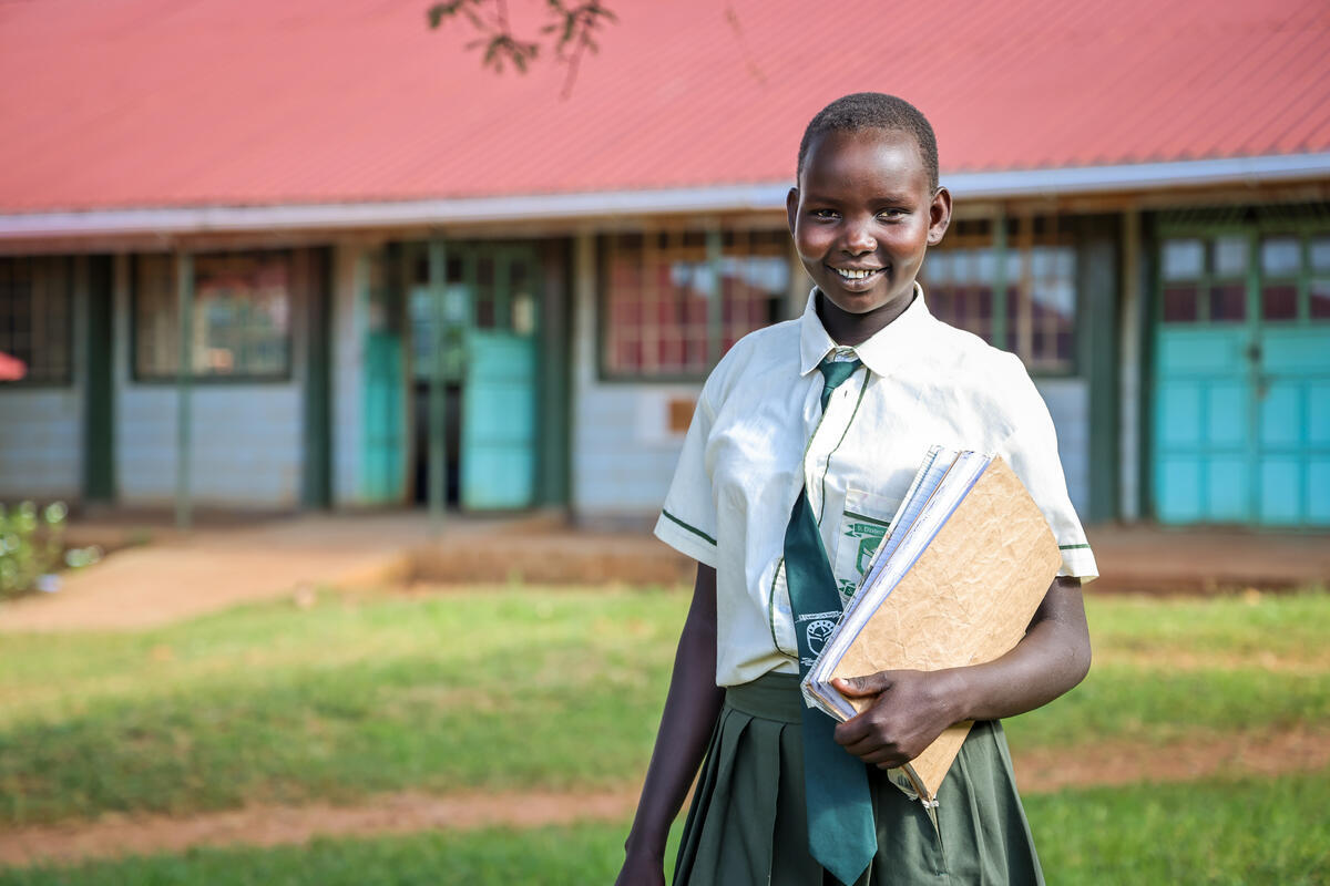 Kenyann teenager smiles in school uniform whilst holding a book