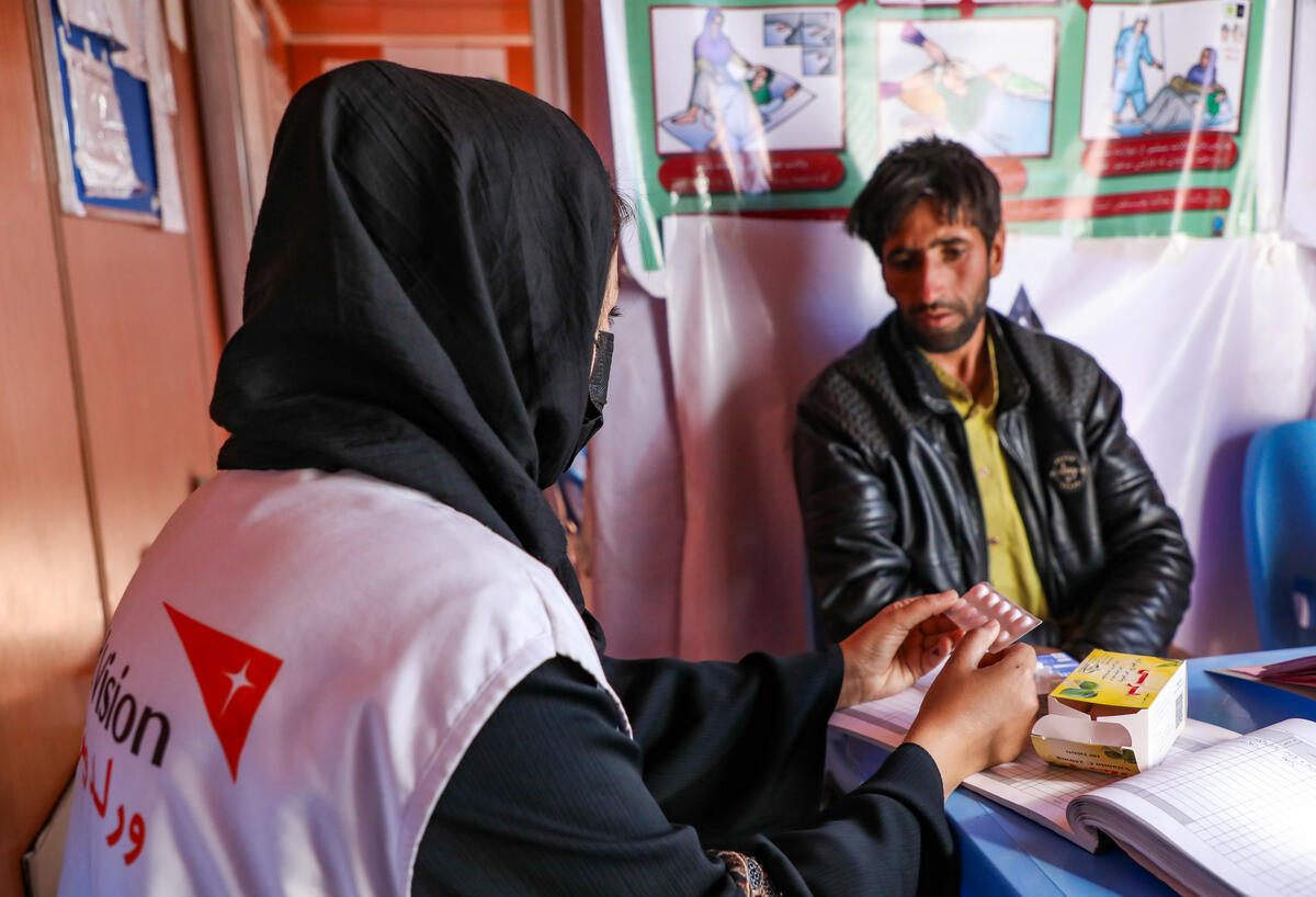 World Vision staff facing Syrian man and showing him medication