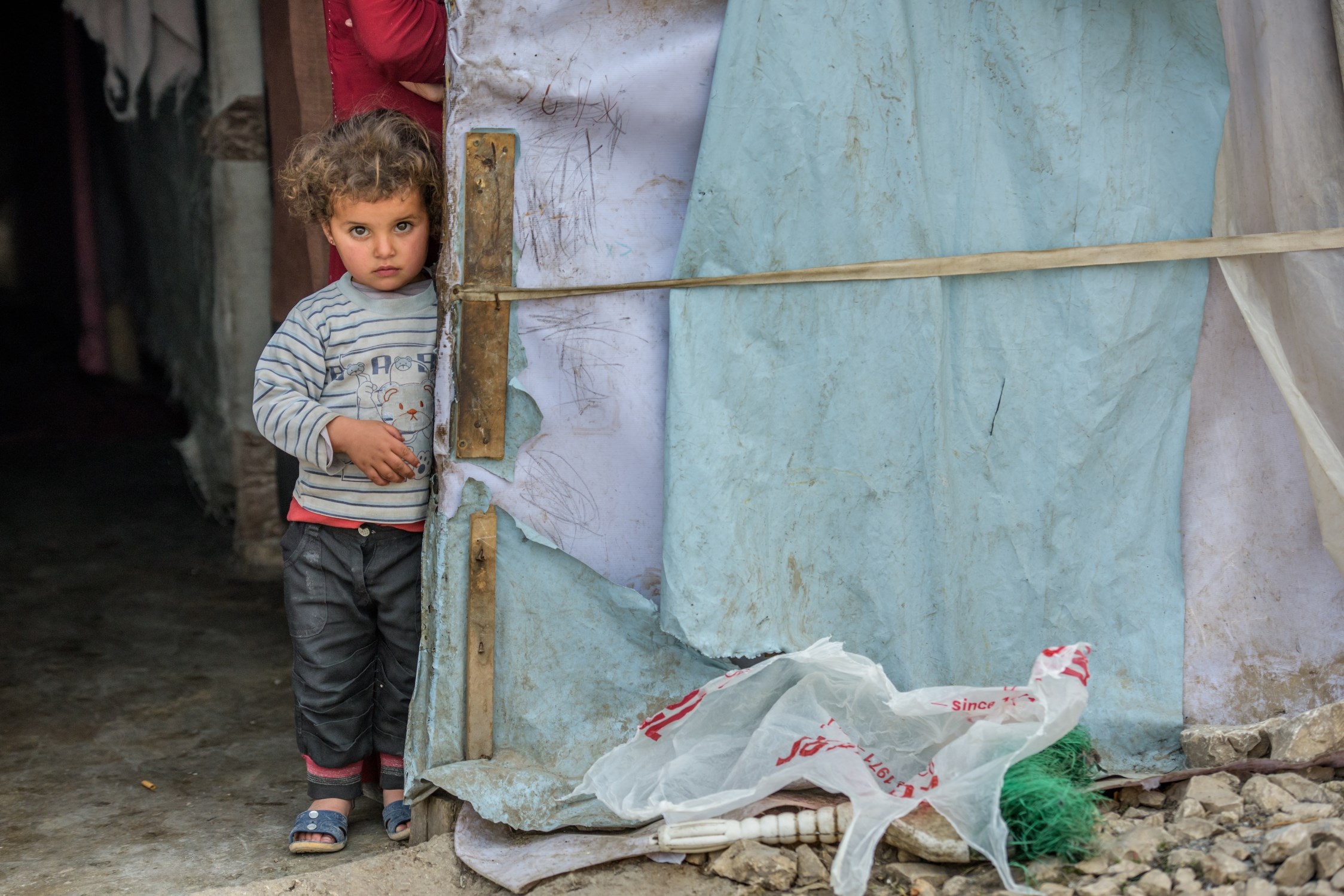 A little refugee from Syria stands in front of a tent in a refugee settlement 