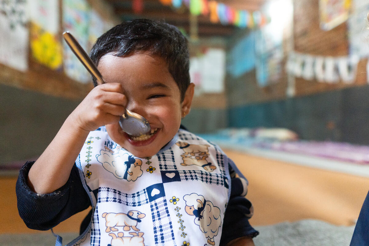 A child in Nepal smiles brightly whilst eating food off a spoon. 