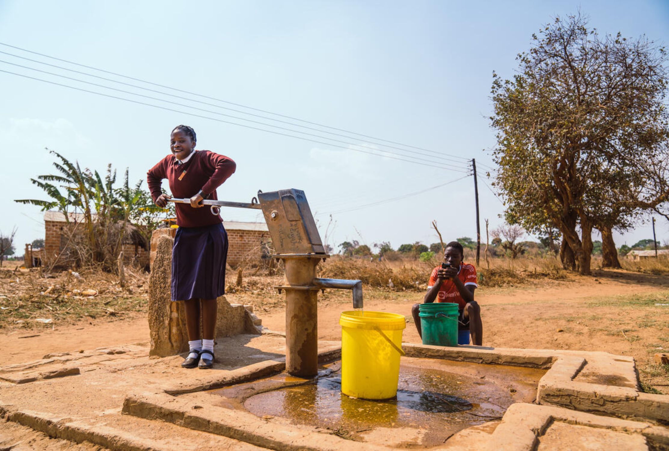 Zambian girl pushing down the borehole's hand pump with all her weight