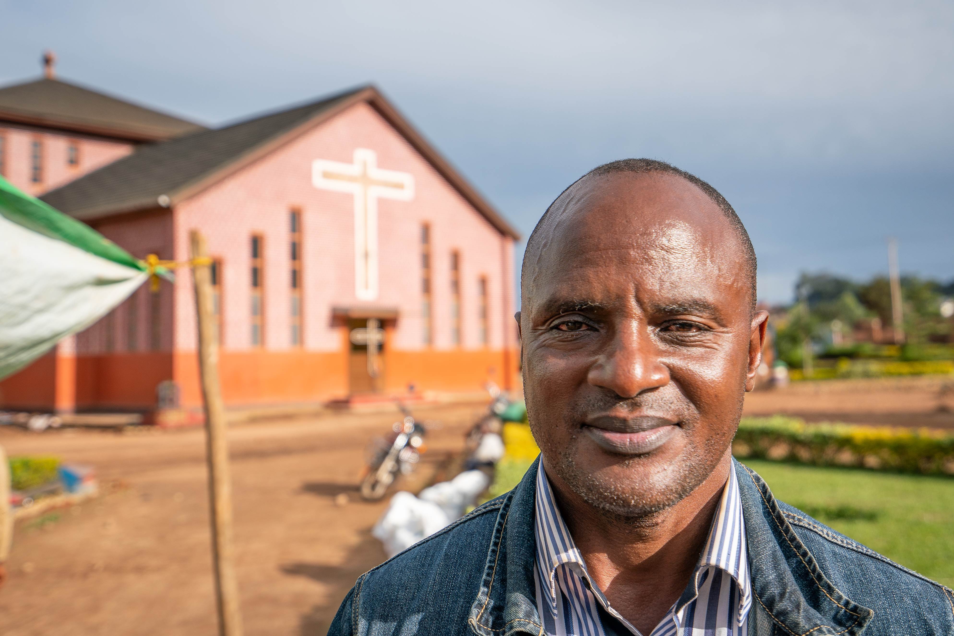 Man from DRC stands outside a church, smiling into the camera