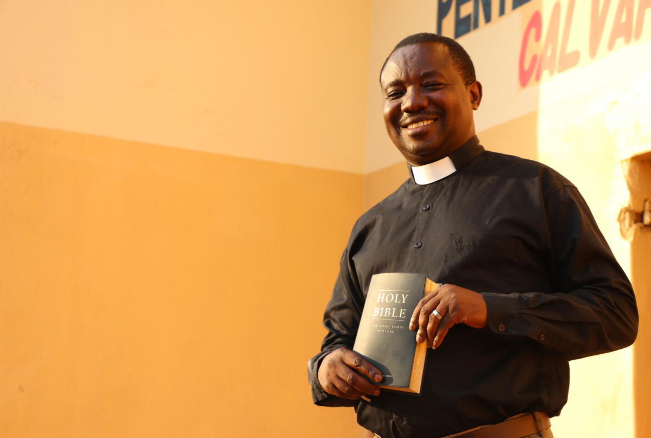 A Zambian reverend smiling at the camera and holding a bible