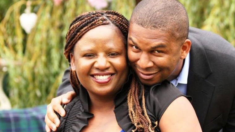 UK woman and man smile into the camera, his arm around her as she sits outside