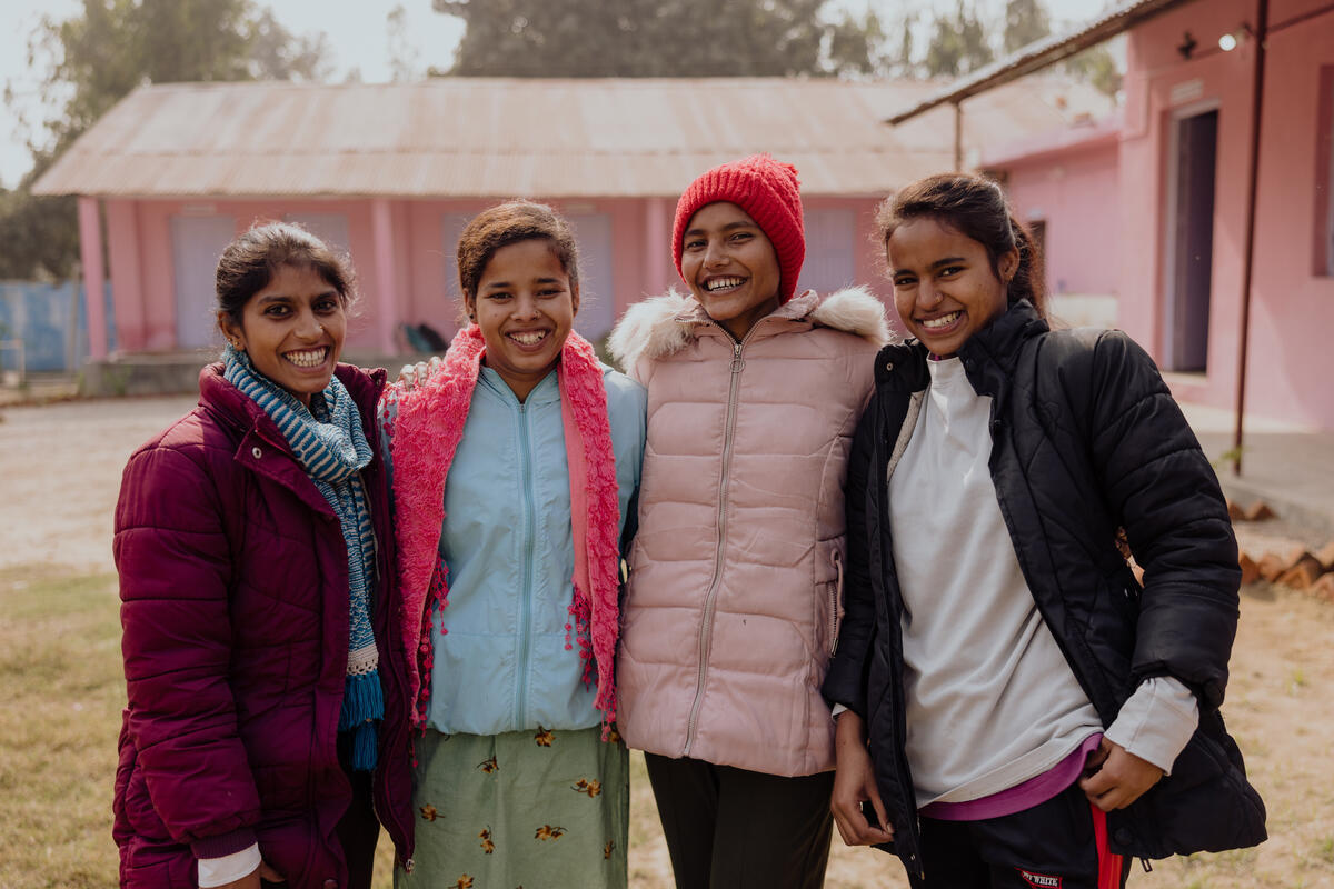 Four teenage girls in Nepal stand shoulder to shoulder smiling at the camera