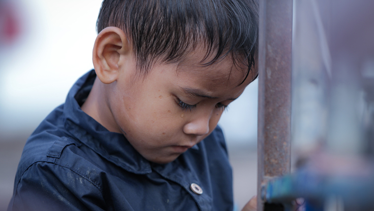 Boy looks sad and looks down as he stands outdoors