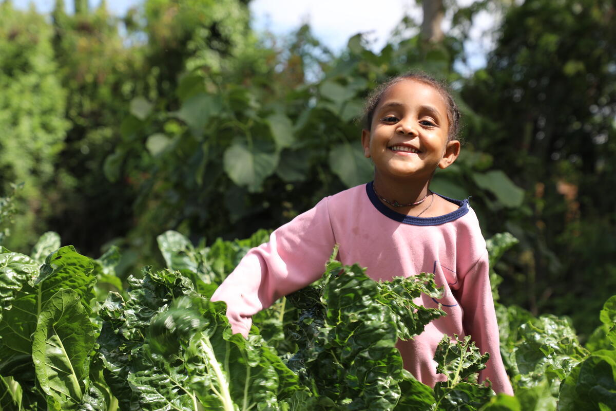 Girl in Ethiopia smiles and touches a flourishing vegetable plant in a garden