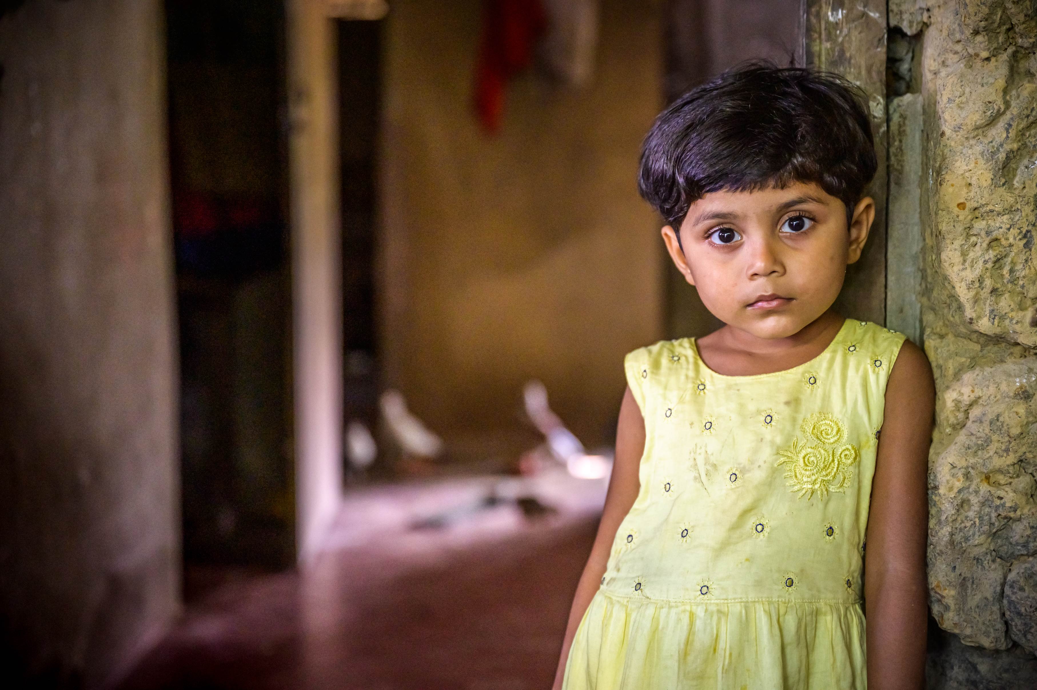 A little girl leans against the doorway of her home in Bangladesh