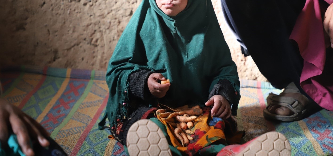 Jamila is sitting on the floor eating carrots that her father had to dig out of a bin.