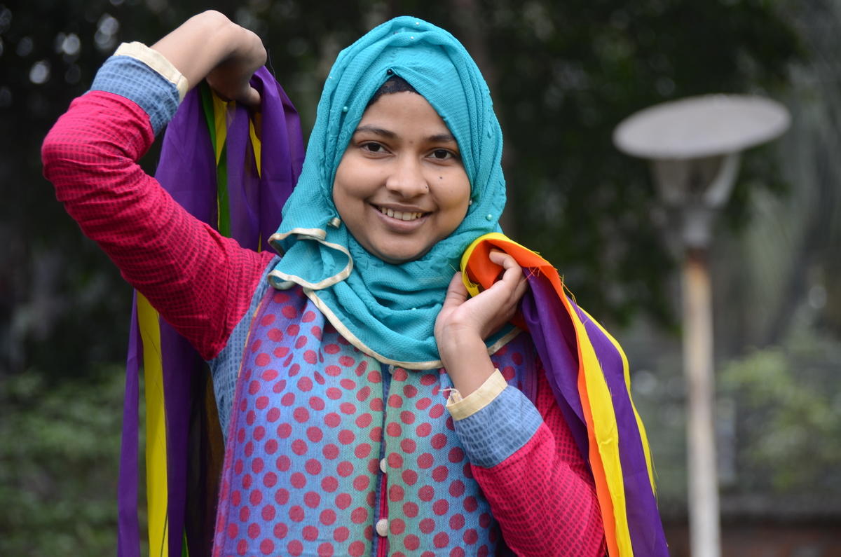 Young teenage girl in bright clothes holding material and smiling at the camera in Bangladesh