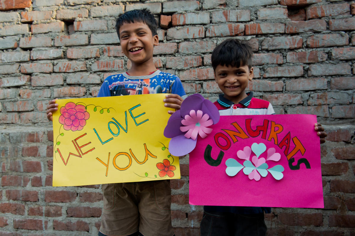 2 young boys in India hold signs saying 'we love you' and 'congrats' for Meghan Markle