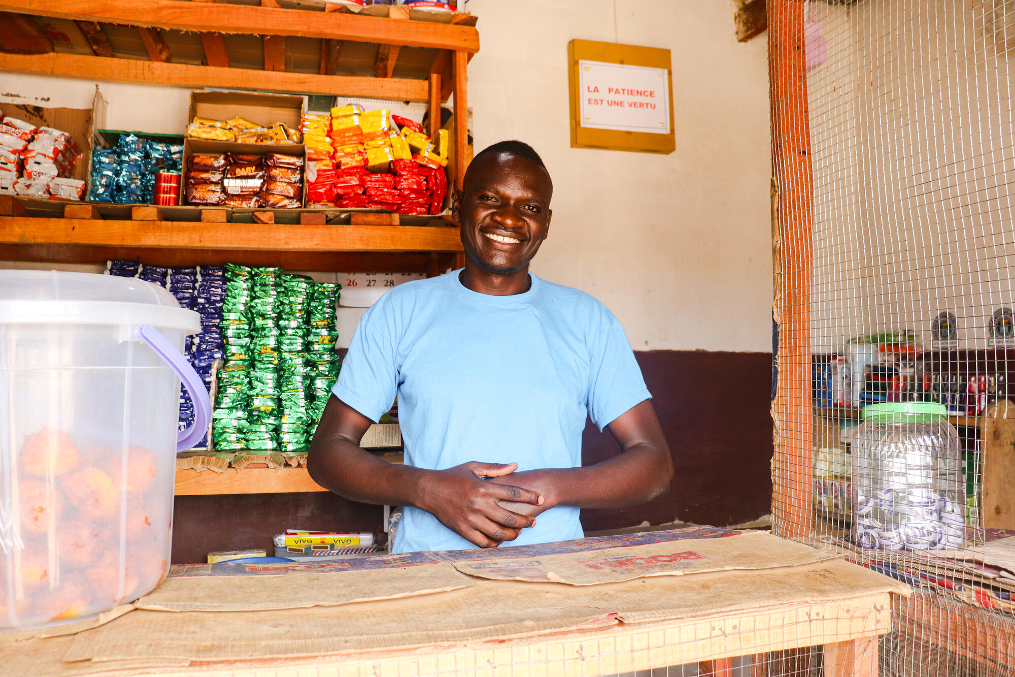 Shop owner from DRC stands smiling behind a wooden counter