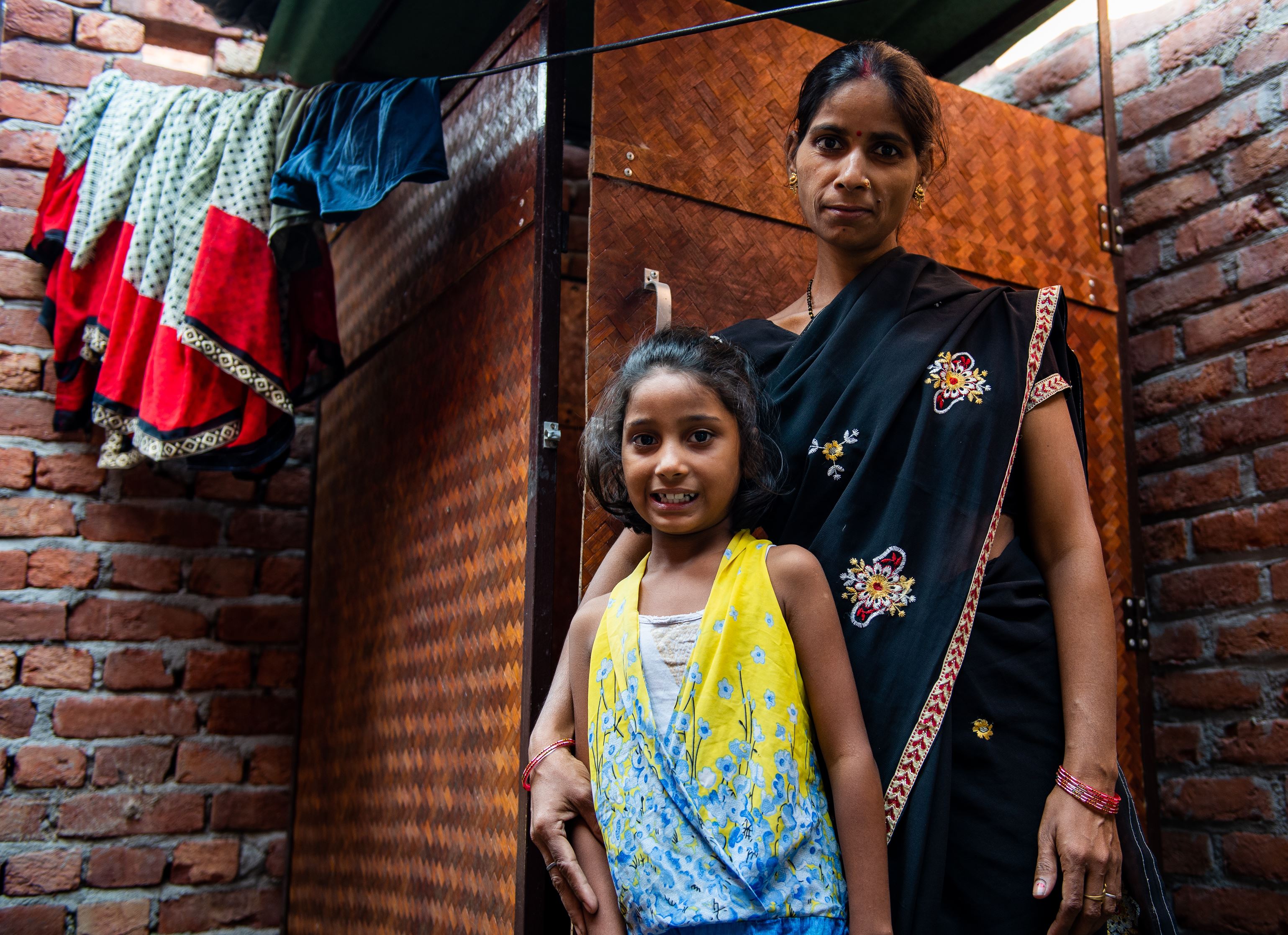 Young girl standing in front of her mother who are standing in front of a toilet cubicle