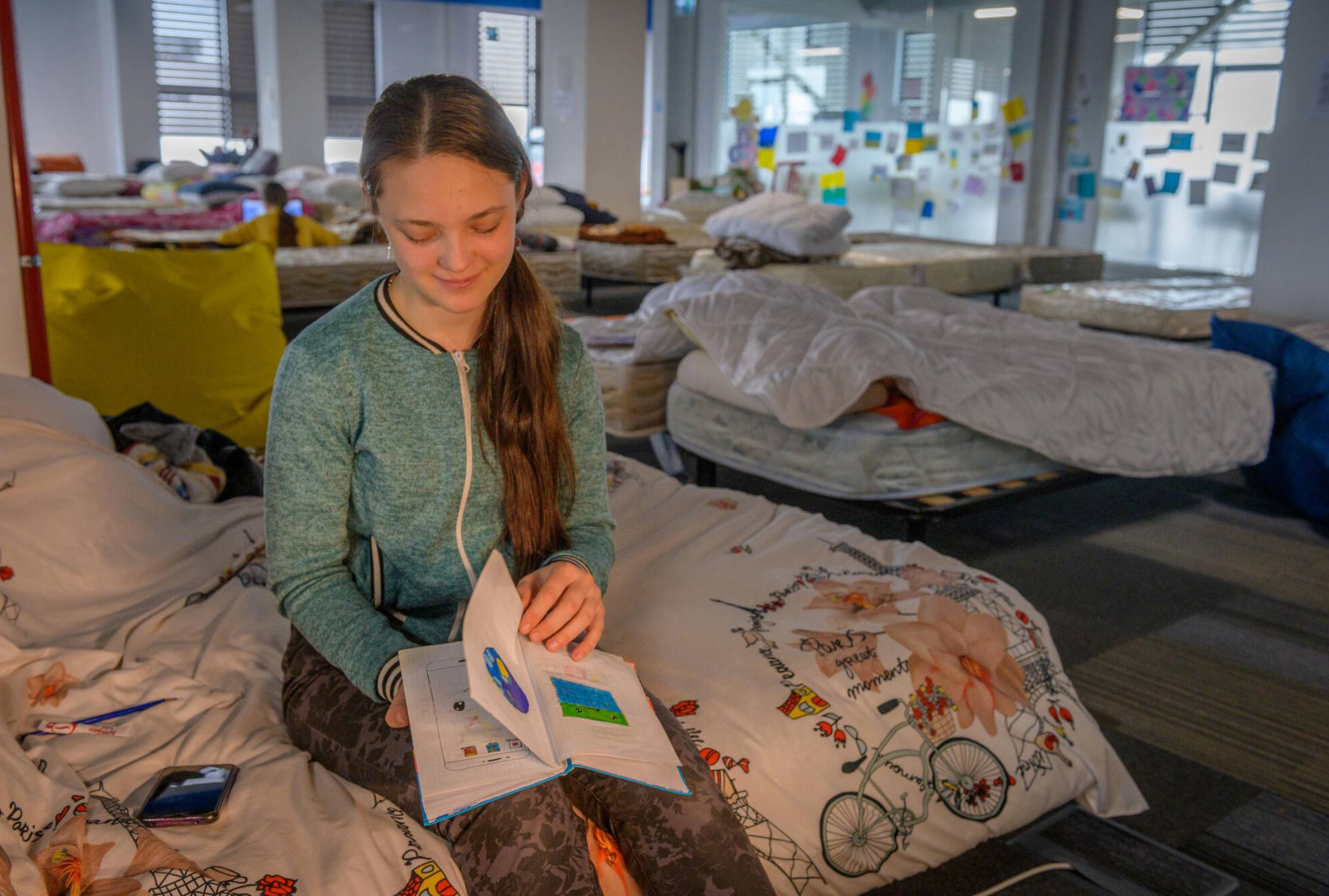 Ukrainian girl reading a book sat on her bed in the refugee centre