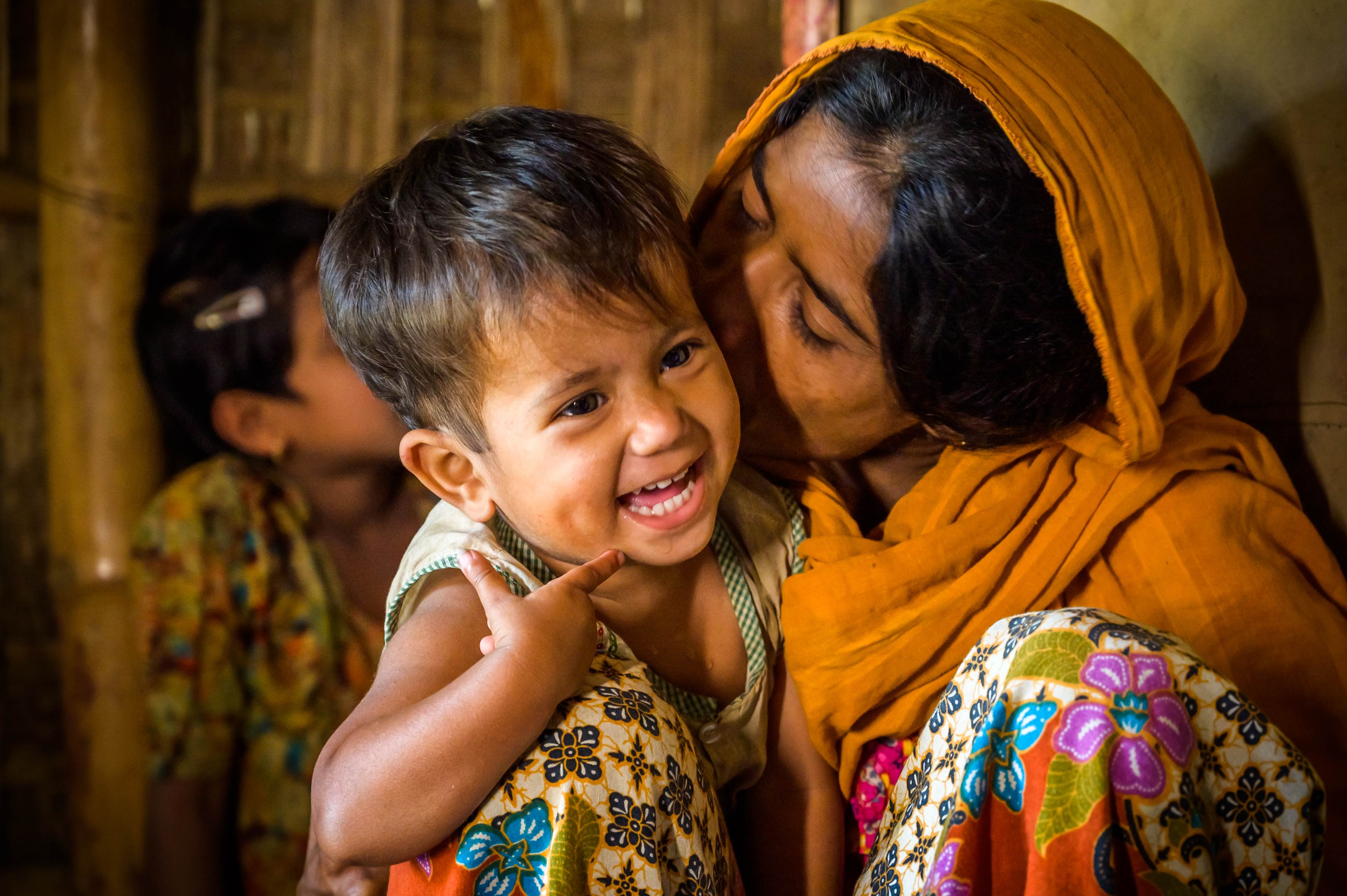 Mother kisses her giggling child in a tent in a refugee camp in Bangladesh