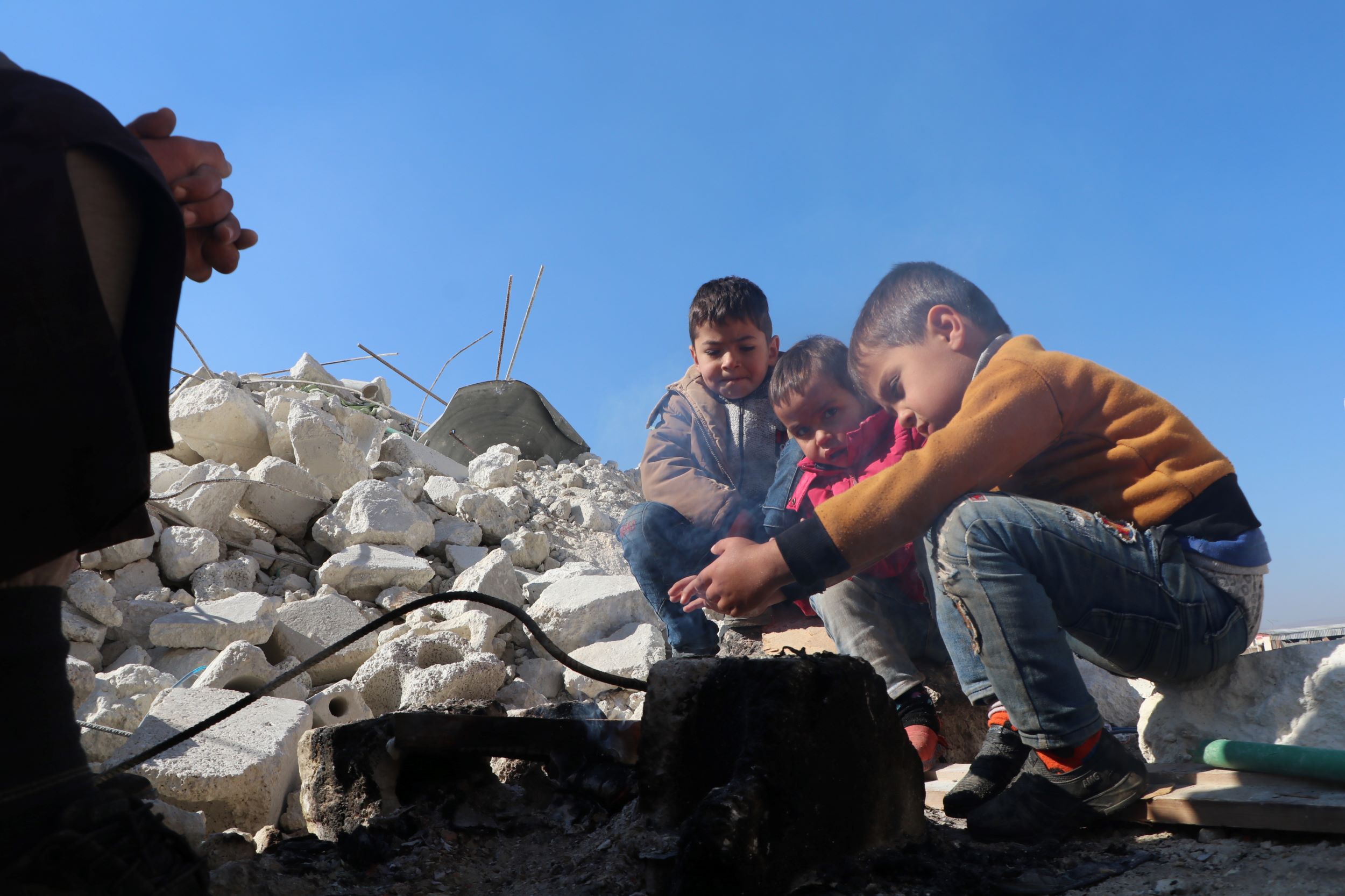 Syrian children keep warm in the shadows of ruined buildings
