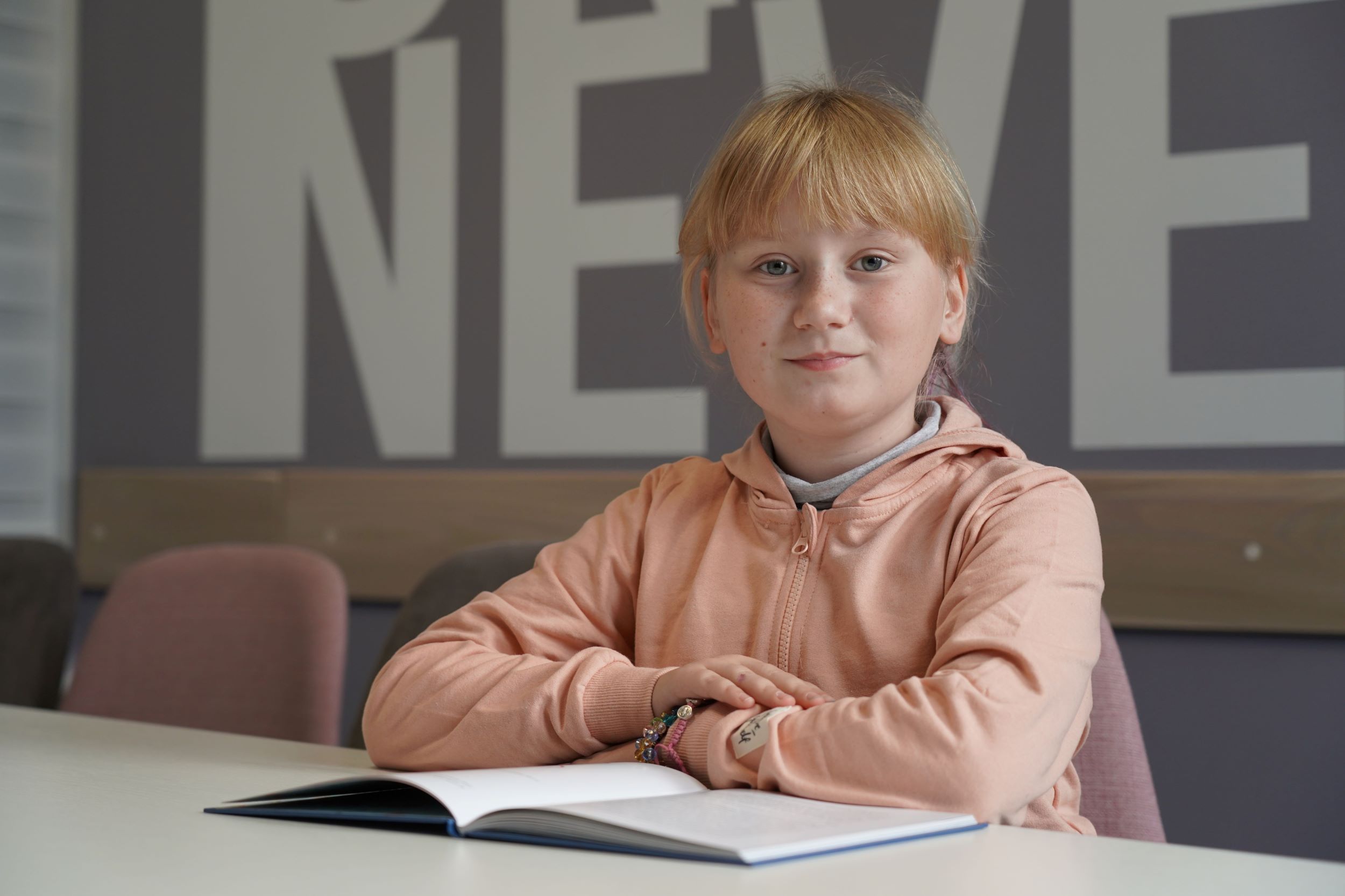 Smiling Ukrainian girl aged nine sitting at a school desk with an open book 