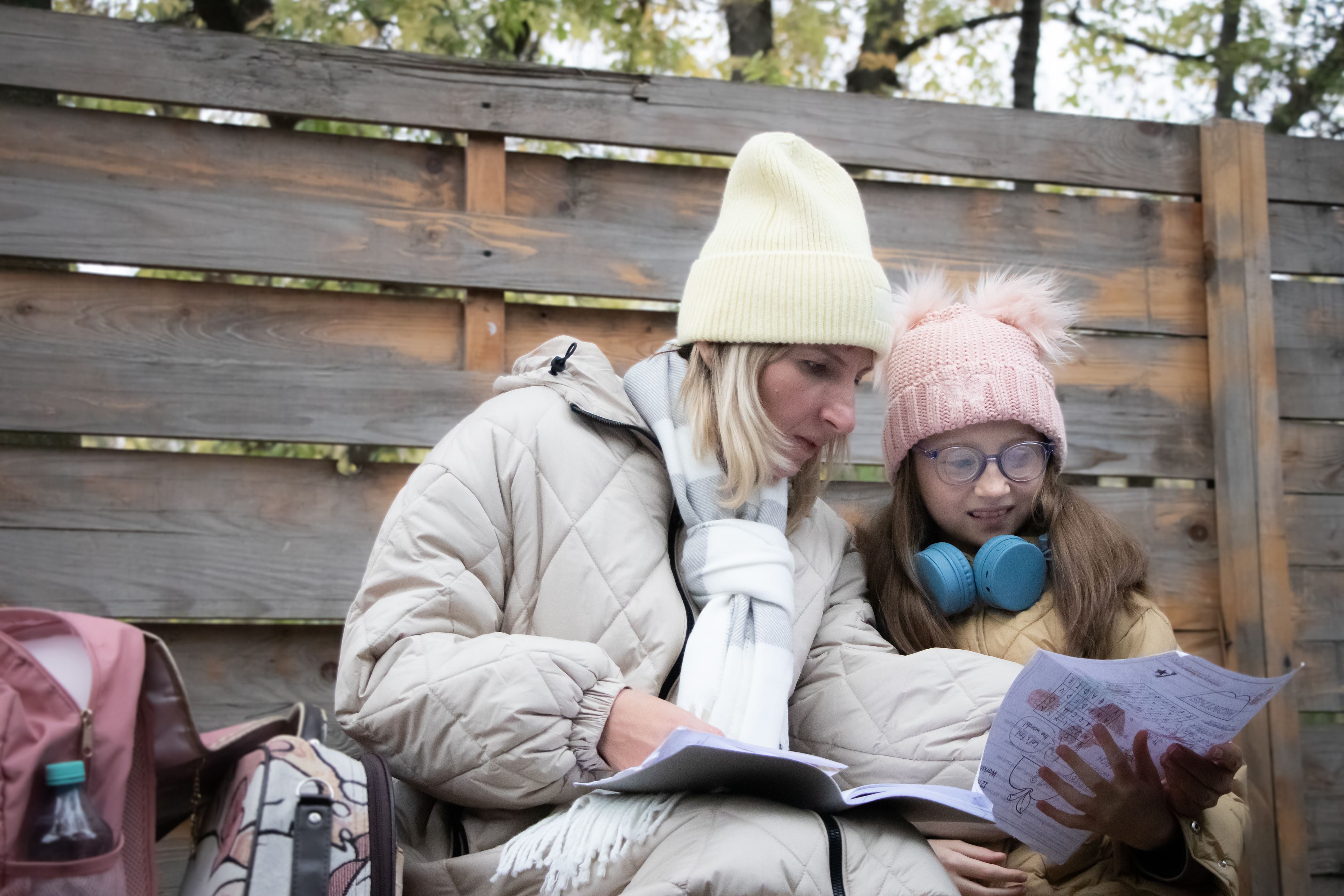 Girl from Ukraine reading with her mother in a refugee camp in Ukraine, wearing winter clothes and hats