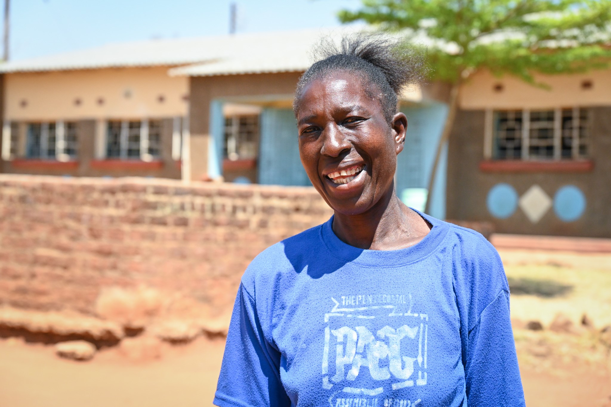Joyce, wearing blue t-shirt, stands in front of the school she founded