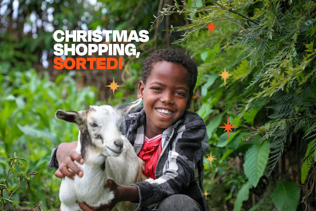 Child from Ethiopia standing outside holding a goat and smiling to the camera