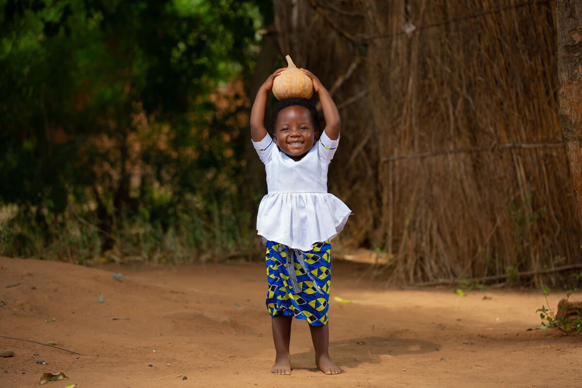 Two-year-old girl in Malawi holds up a home-grown pumpkin