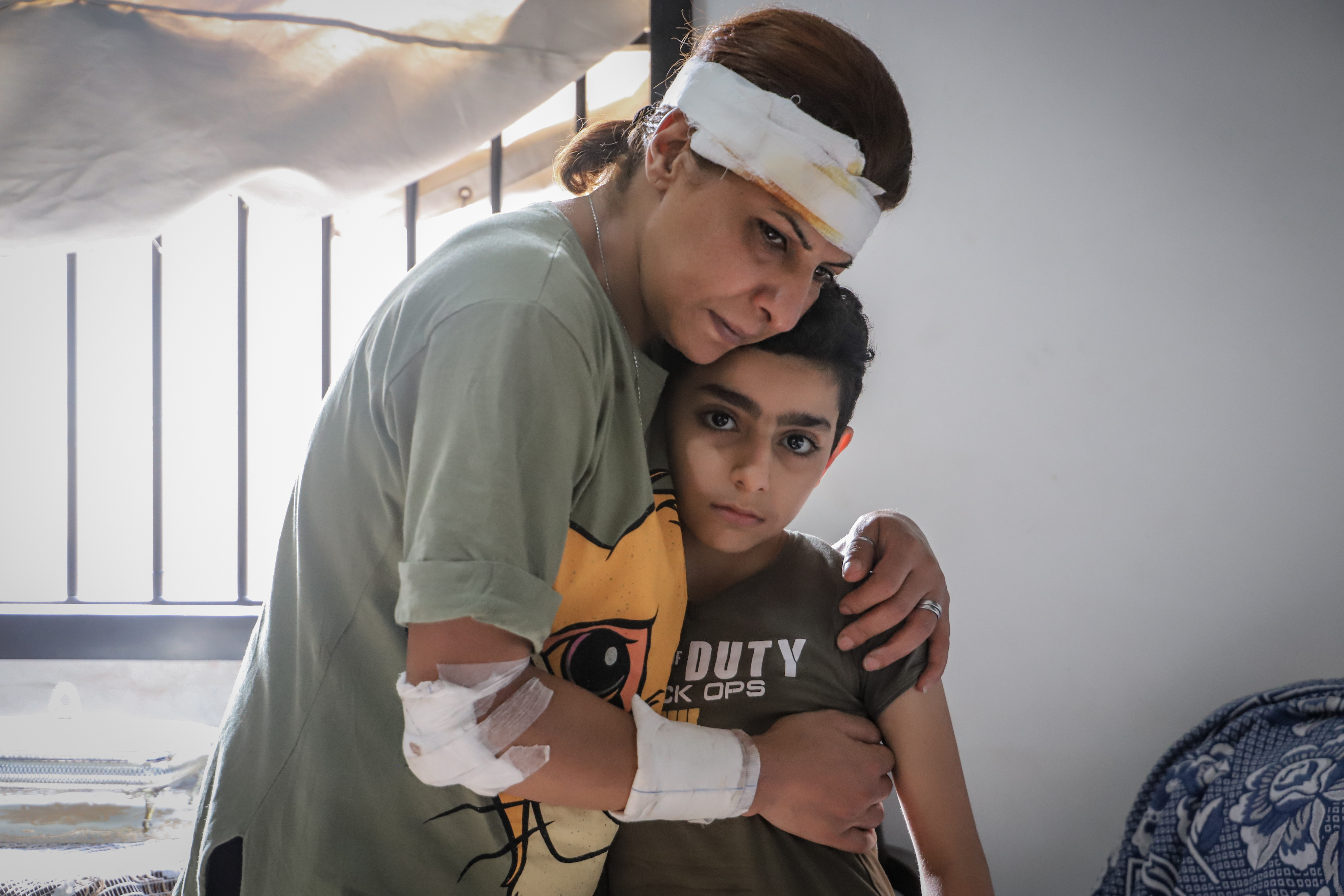 Woman with bandage across her head cradles a boy in a room in Beirut, Lebanon after the 2020 explosion