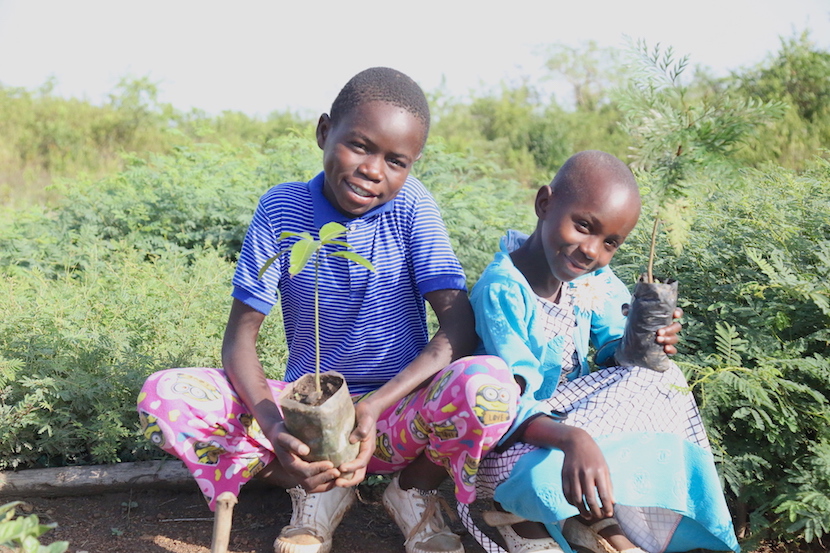 Two young girls crouch in a field in Kenya - proudly show the crops their family has grown