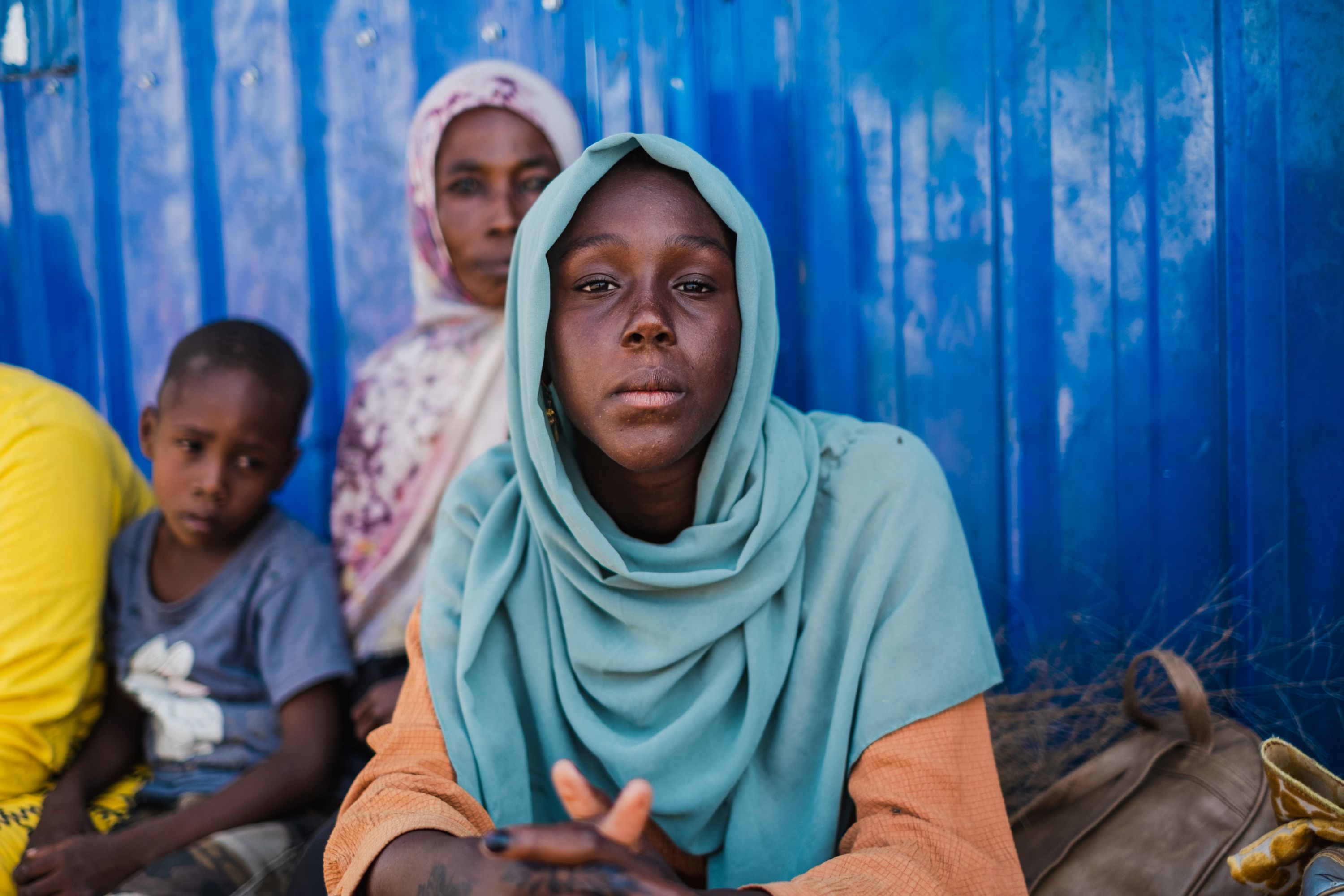 Sudanese refugee girl wearing light blue headscarf, pictured with family members at a transit centre in South Sudan