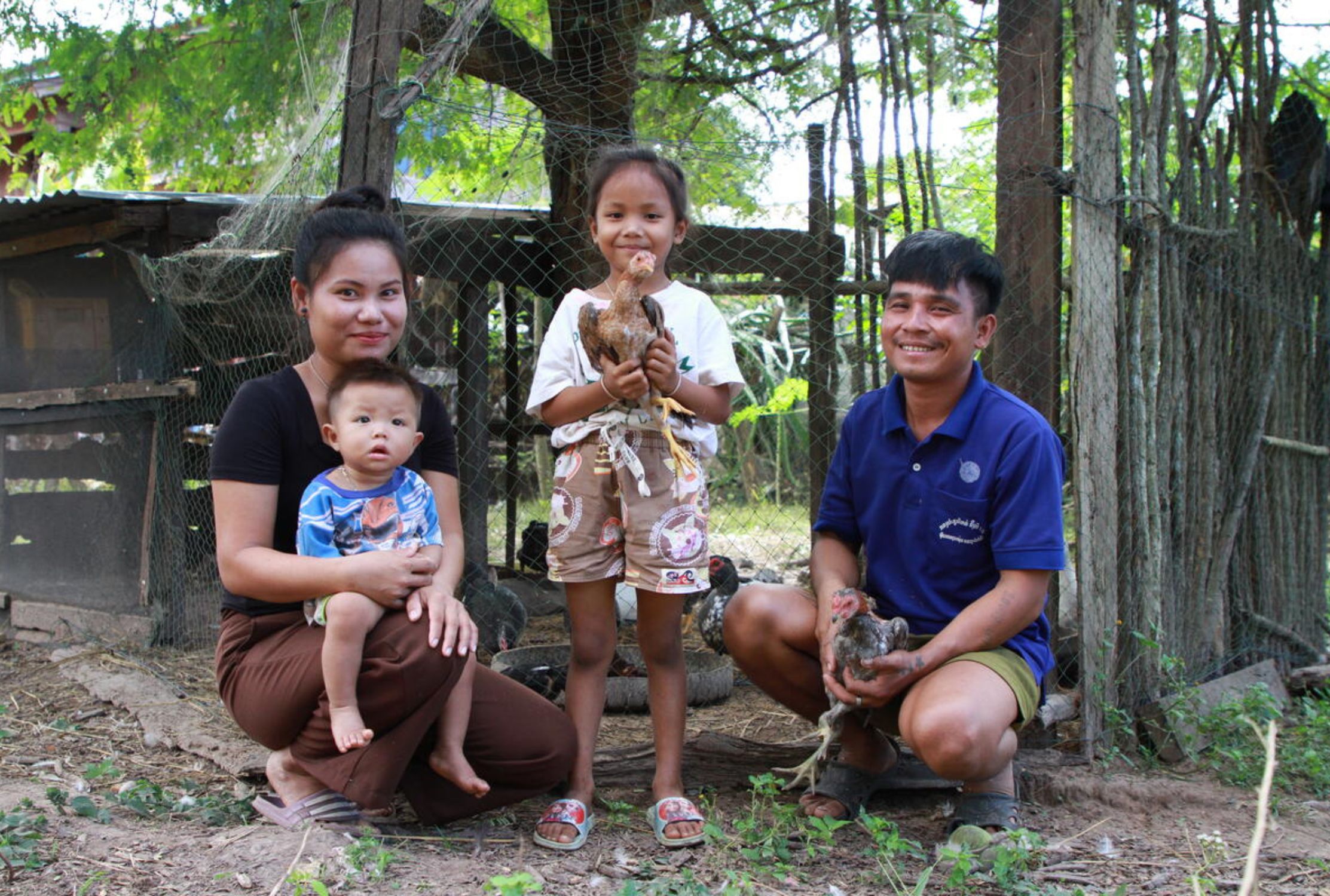 Family from Laos outside the chicken coop, the daughter is holding a chicken and smiling to the camera