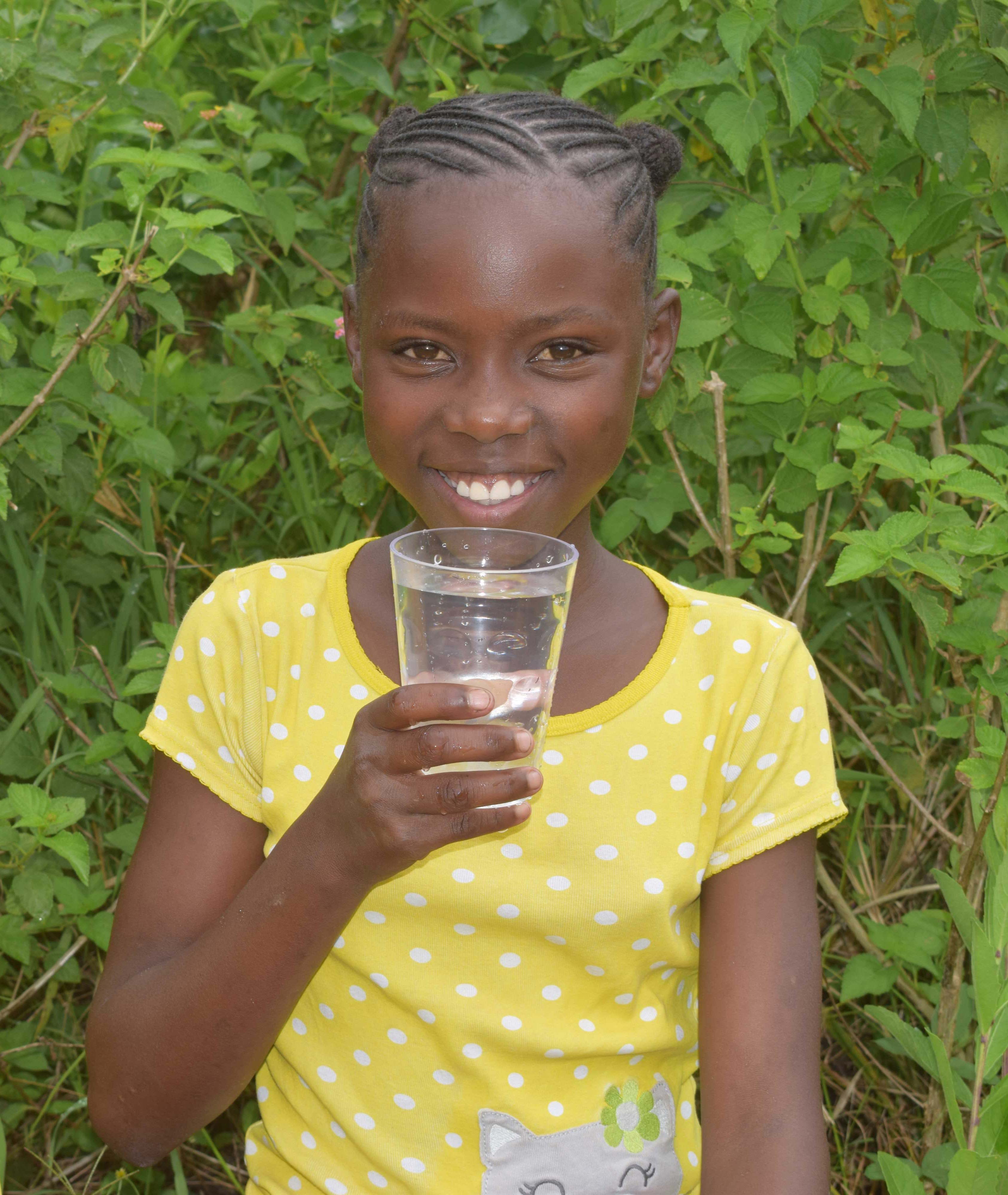 Girl from Kenya smiles broadly as she holds a glass of clean water in a cup