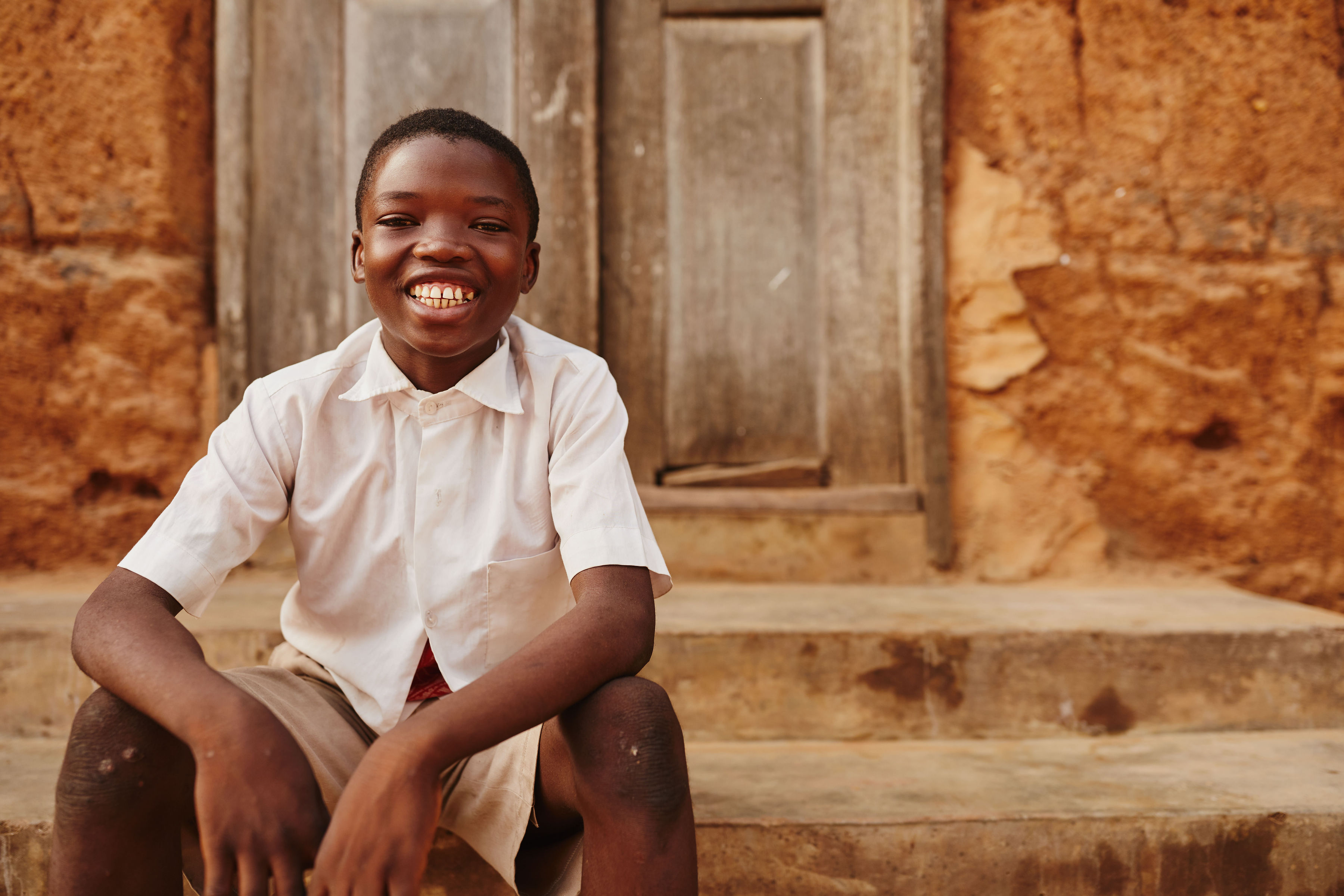 Child in Ghana smiles as he sits on a step outside a building