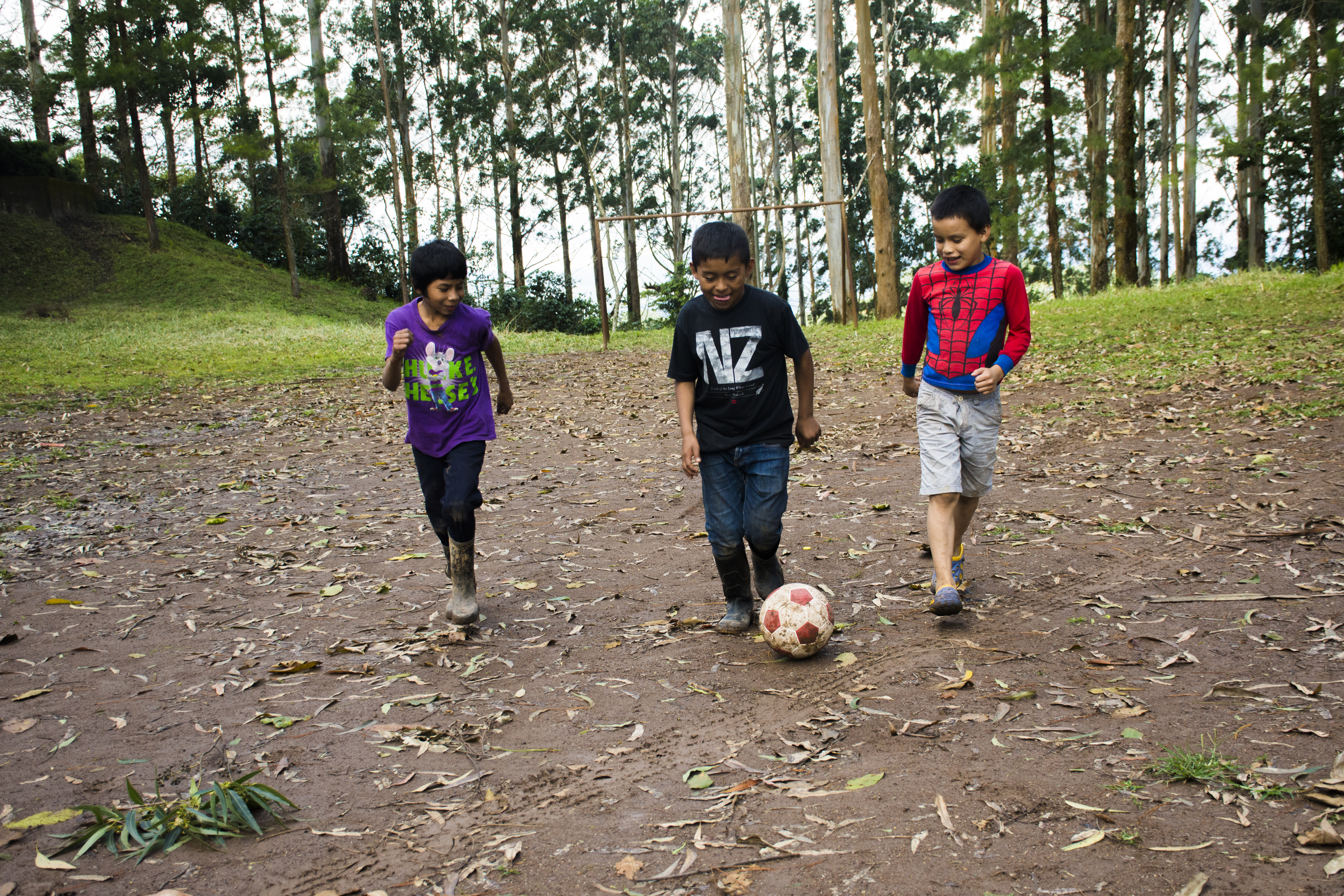 Three boys run through a forest in Nicaragua, laughing as they kick a football around