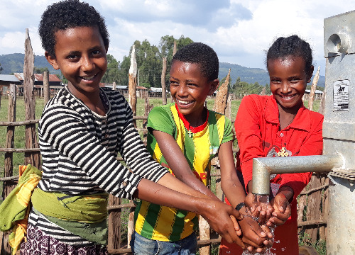Three boys at a water tap.