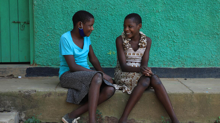 Twin sisters Rebecca and Ruth, sit on the steps outside their home together, in Uganda