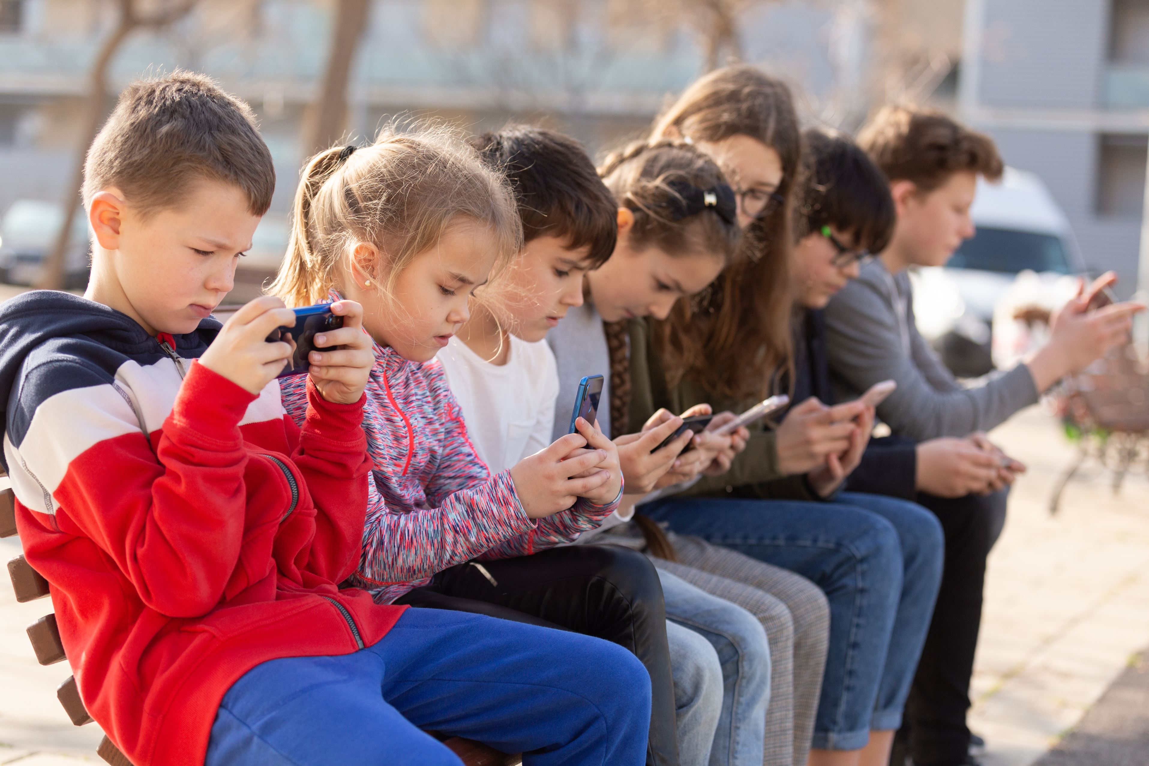 Children sat on a wall outside, all using smartphones