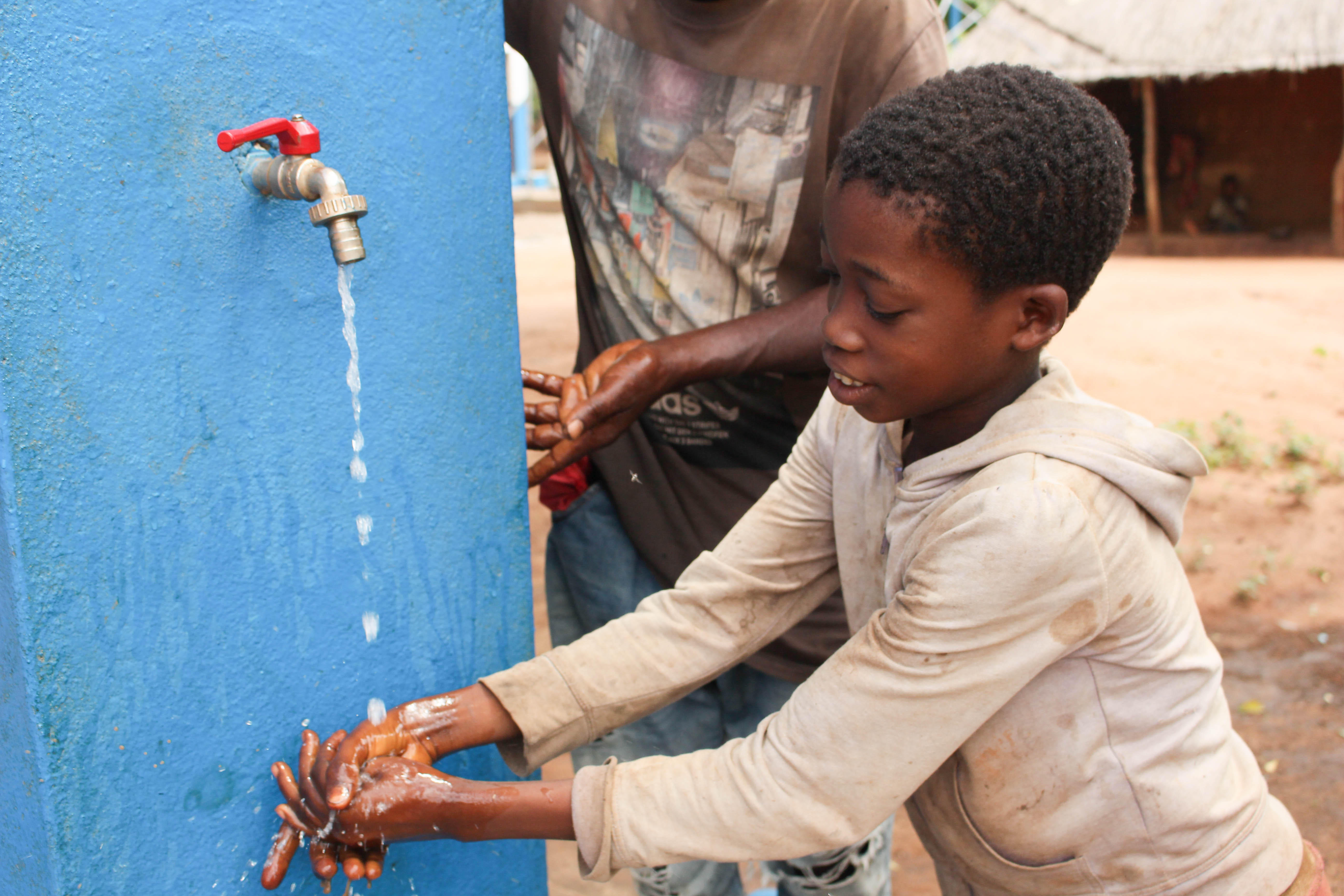 Dércio drinks clean water from the tap with the help of his father, Silvério.