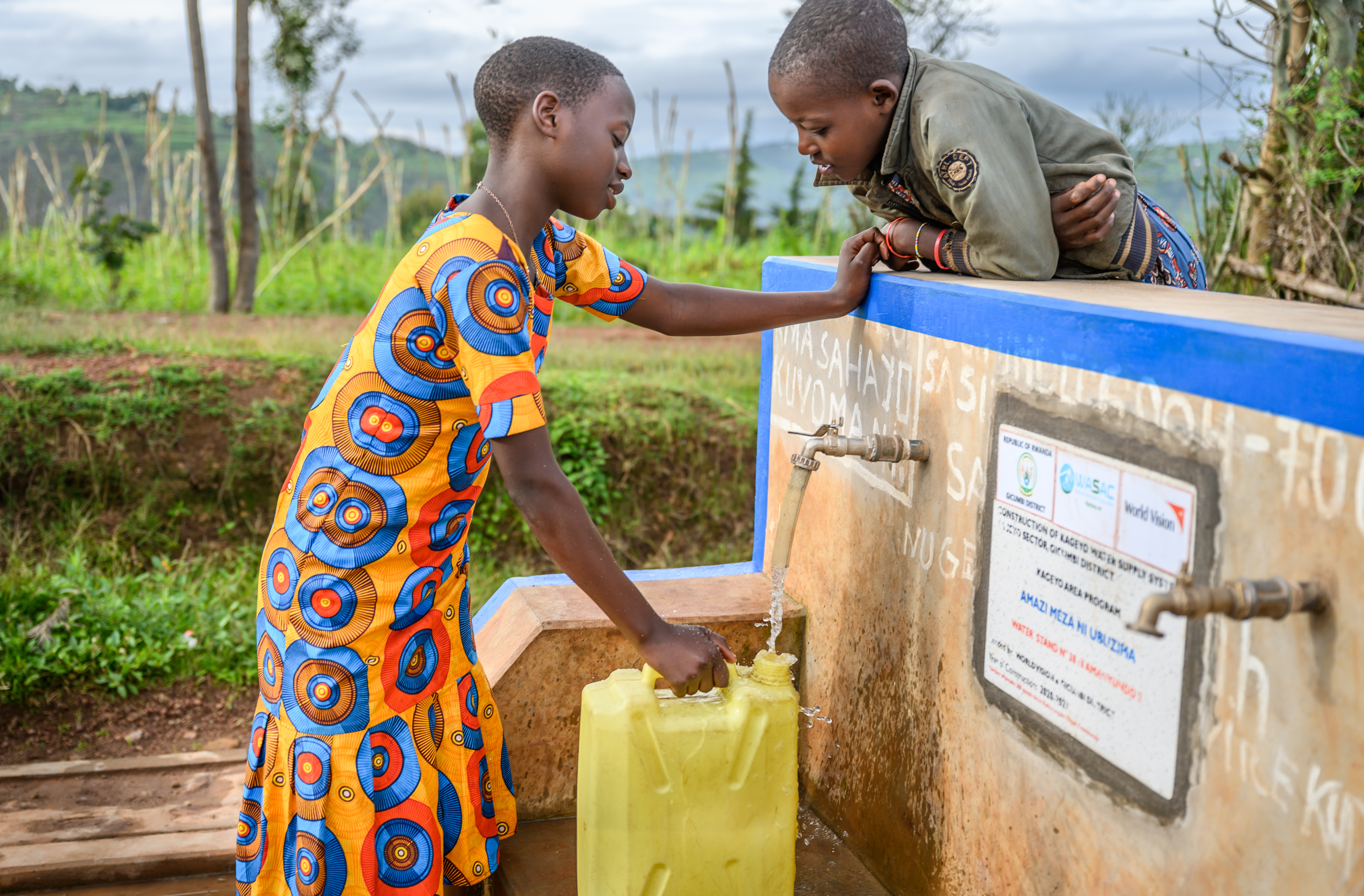 Merci, in a colourful dress with African print, fills up a jerrican at one of the communal taps while her best friend is watching.