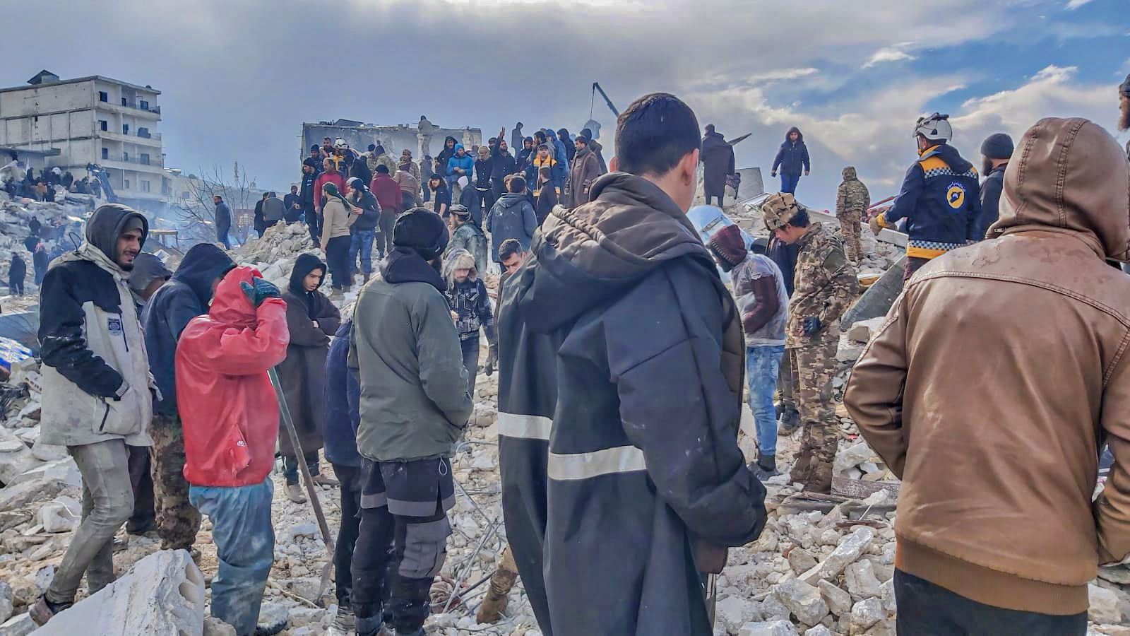 A crowd of people in Syria standing over rubble, watching a rescue operation underway after the earthquake