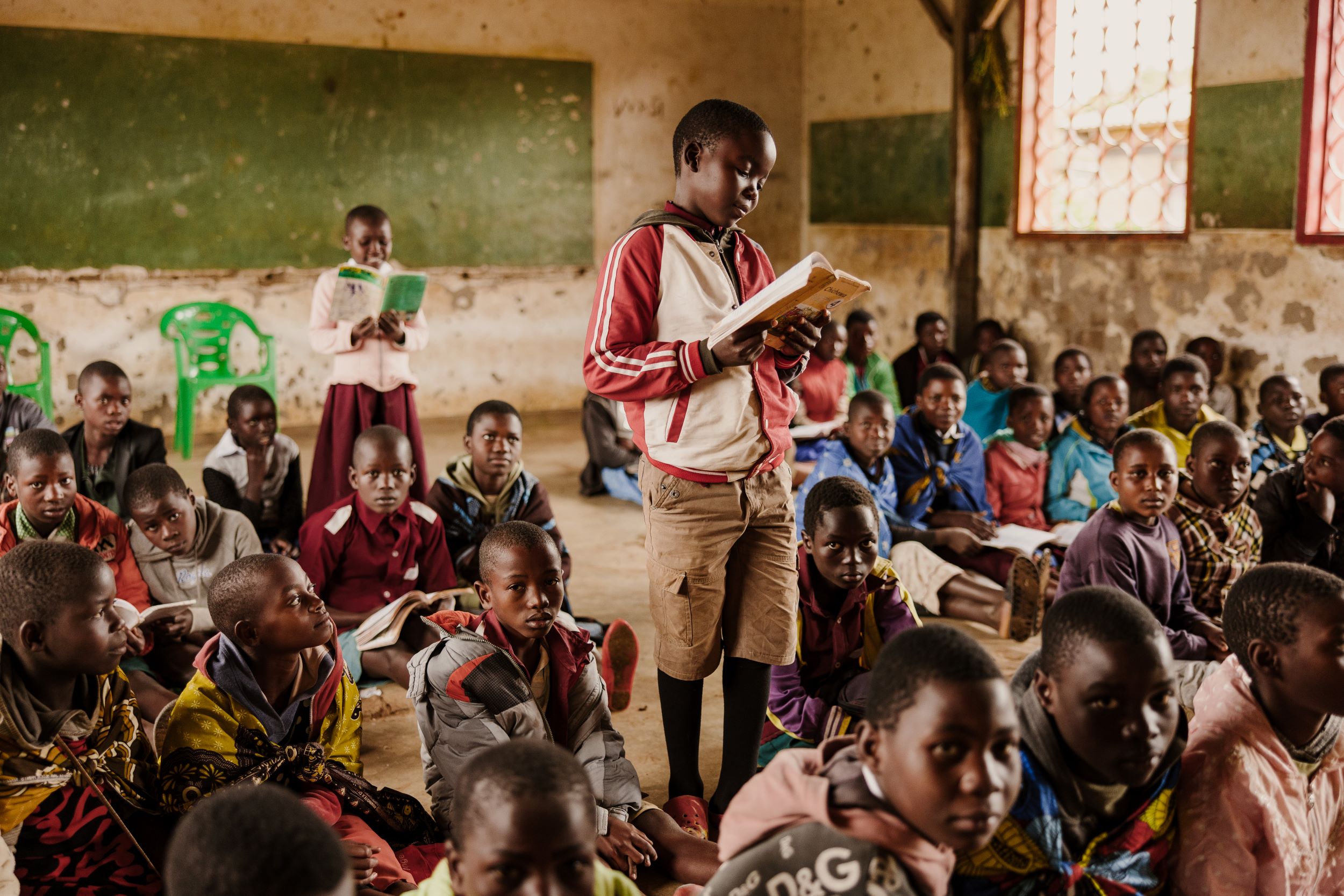 Boy from Malawi standing with open book among fellow classmates