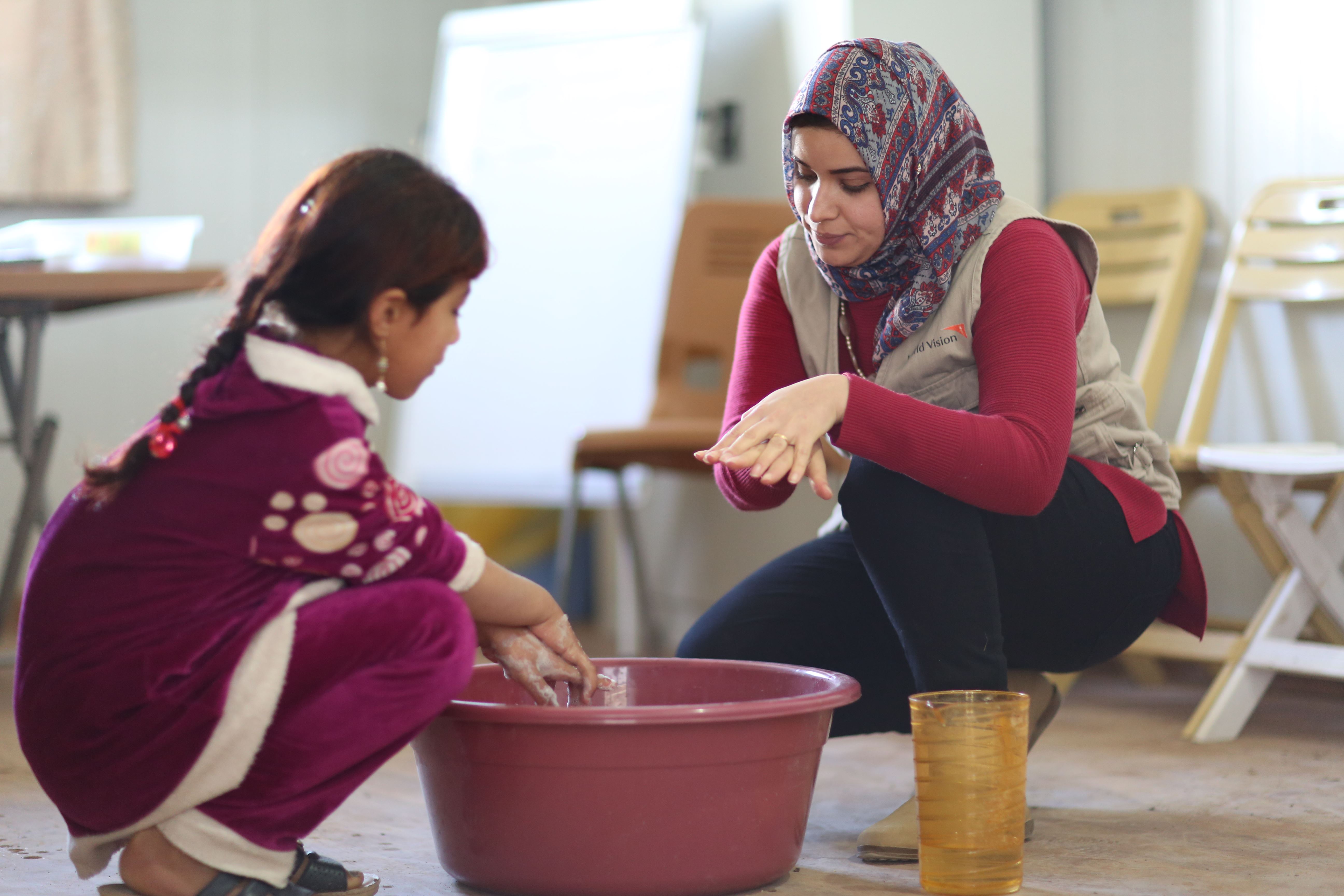Woman and girl in Iraq clean hands in a waterbasin indoors
