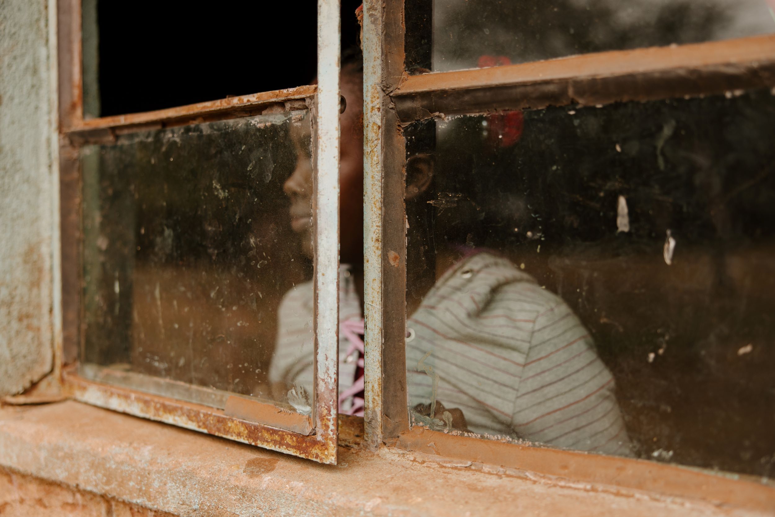 Kenyan girl looking out window. Face obscured by window frame to protect identity.