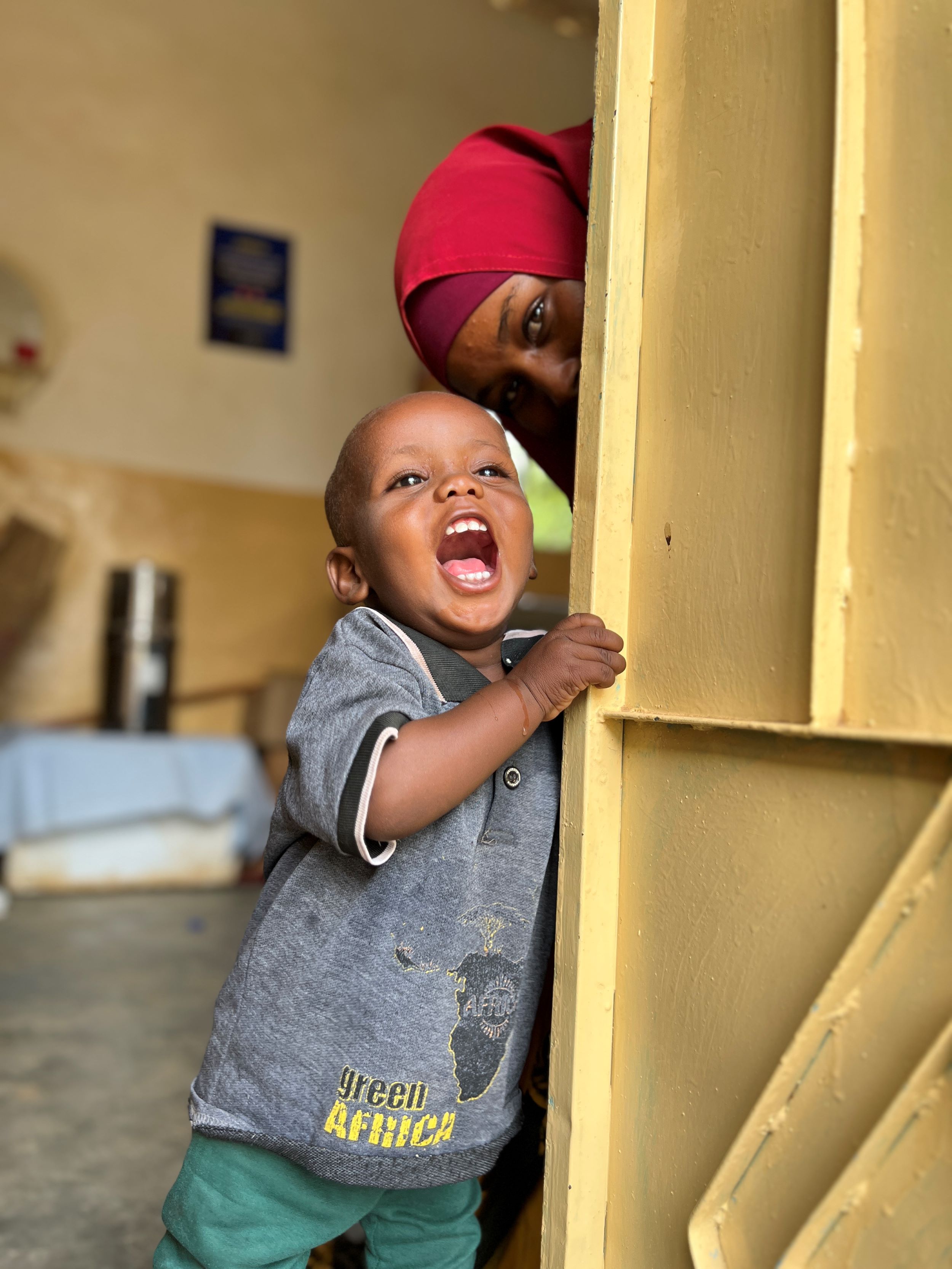 Somali boy in grey t-shirt smiling with his mum behind him