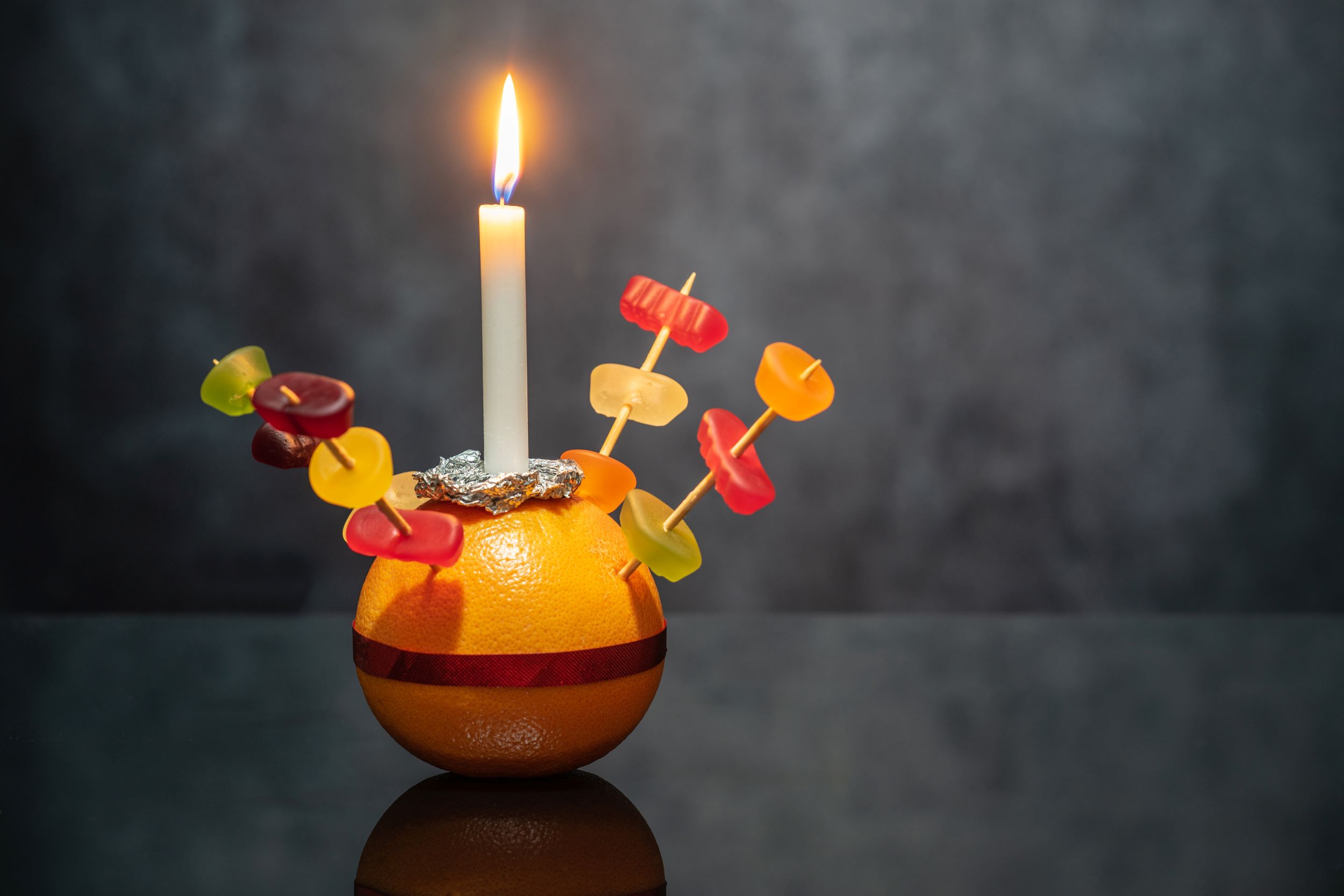 Christingle orange with sweets, ribbon and lit candle