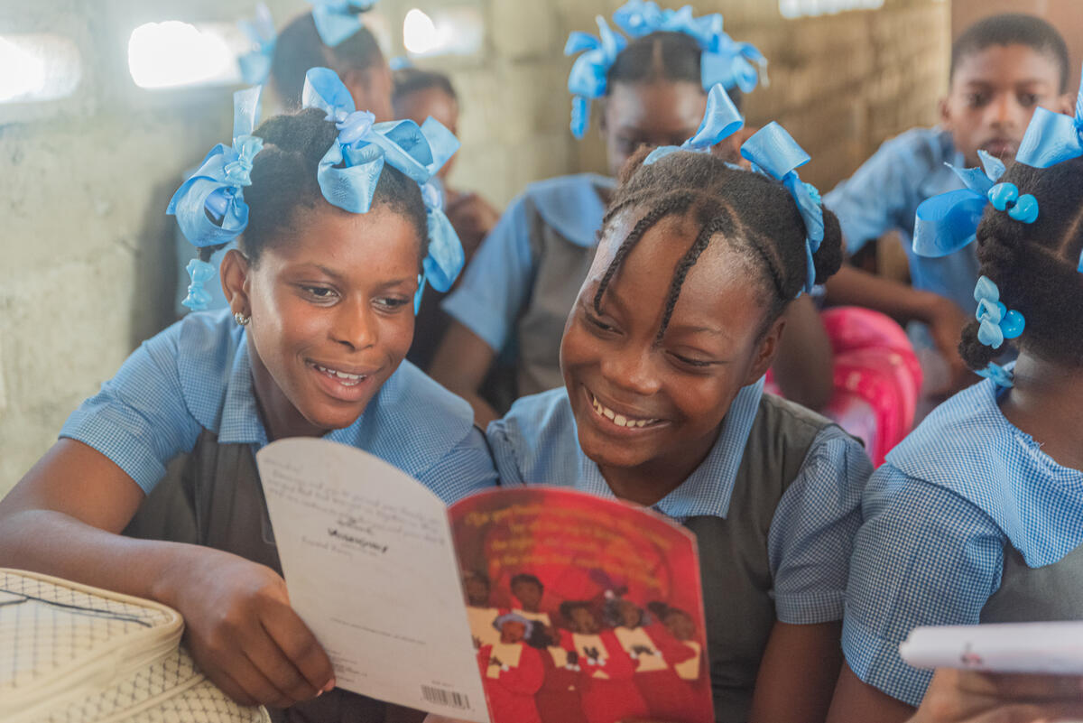 12-year-old girl from Haiti reading a card from her sponsor with her friend in school
