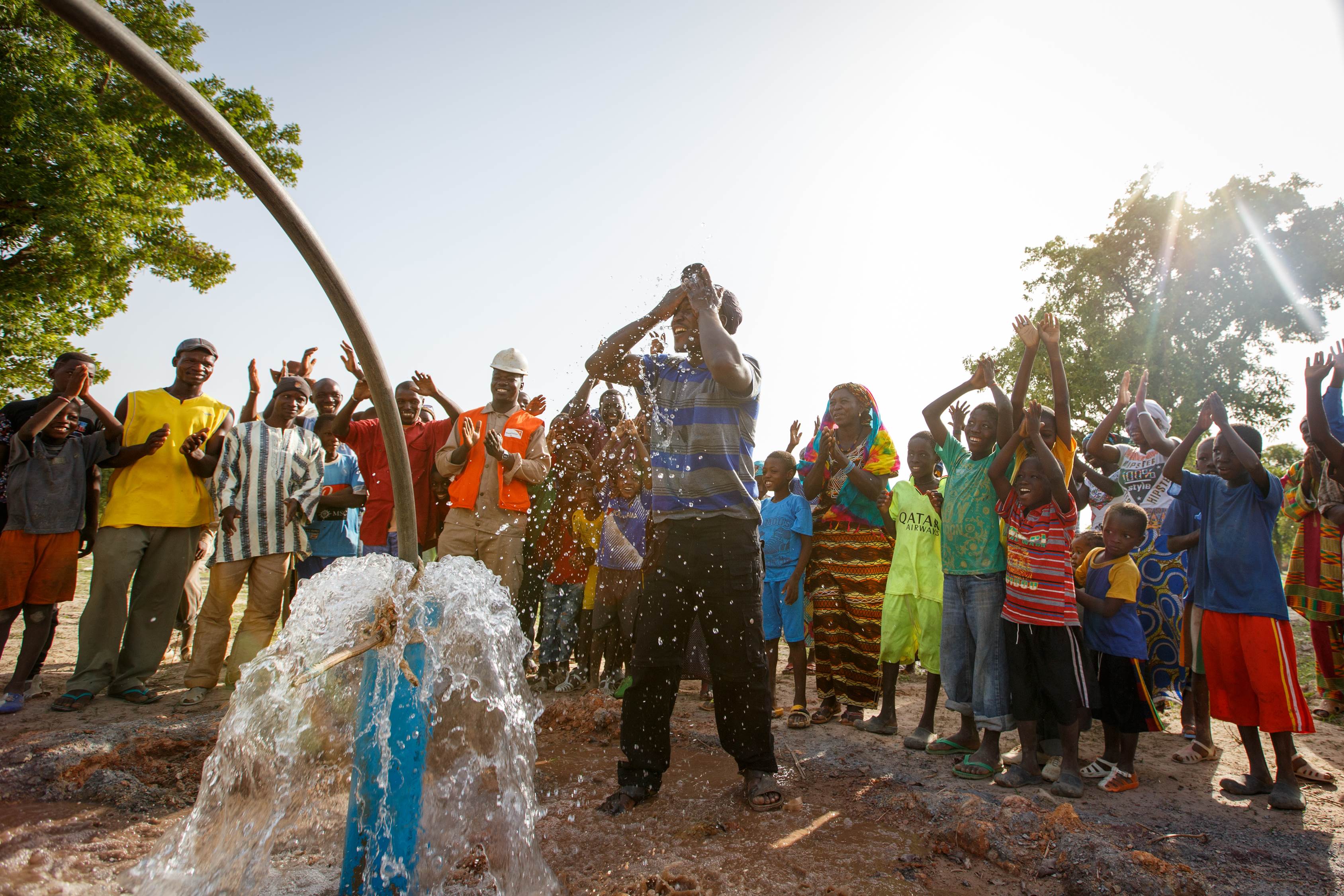 A community in Mali celebrates, dancing and raising arms skyward in front of a newly working borehole in Mali
