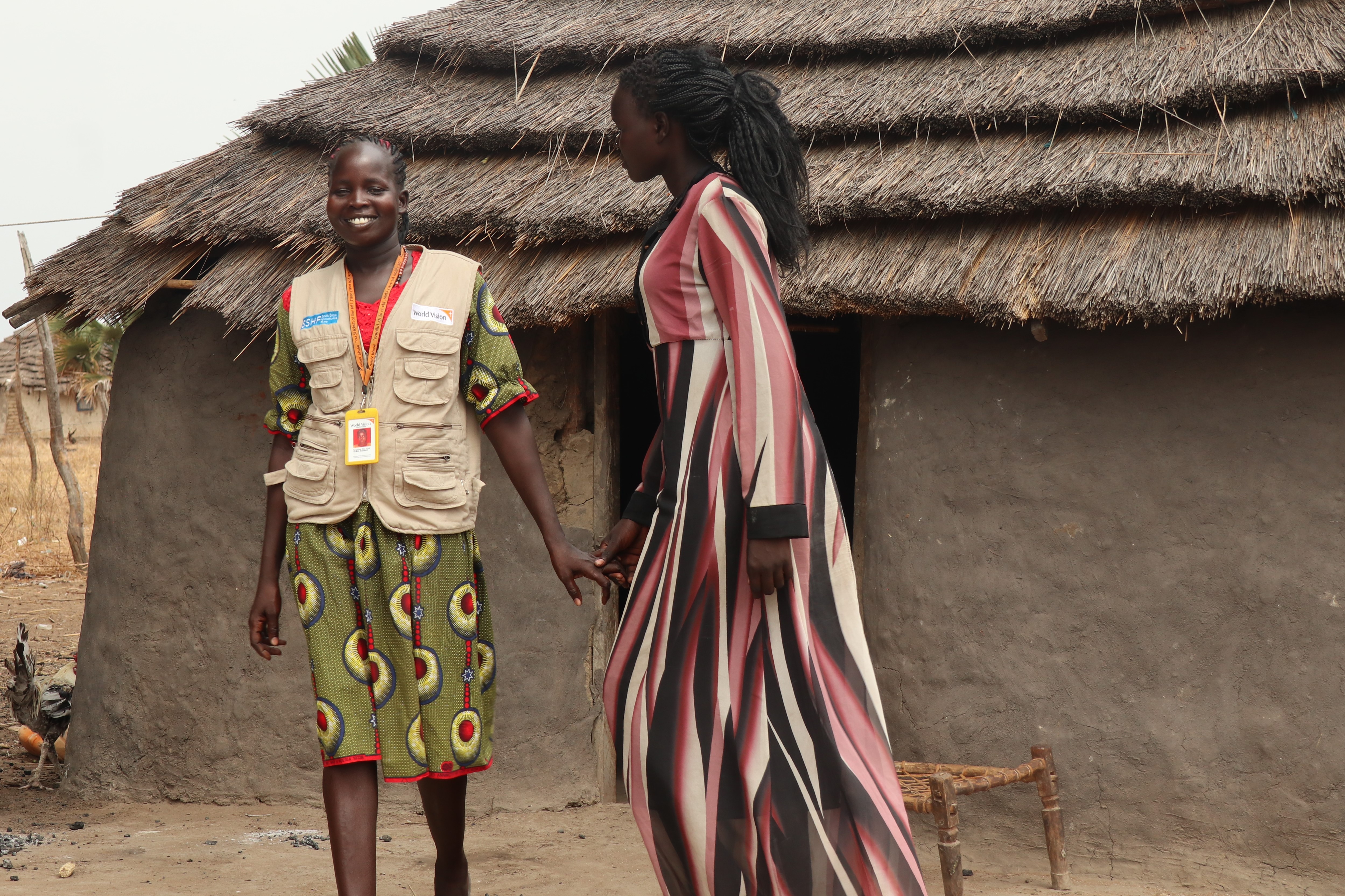 Katina and her World Vision social worker Pasquina smile and chat in front of a house
